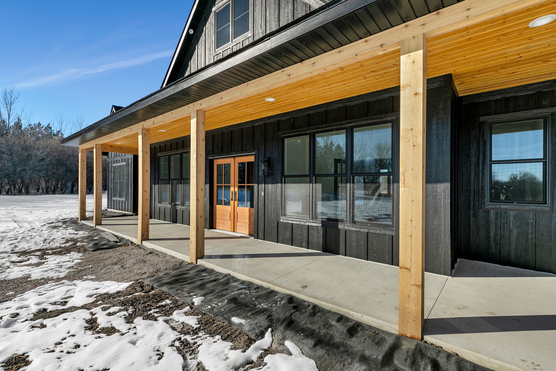 A large house with a porch and snow on the ground in front of it.