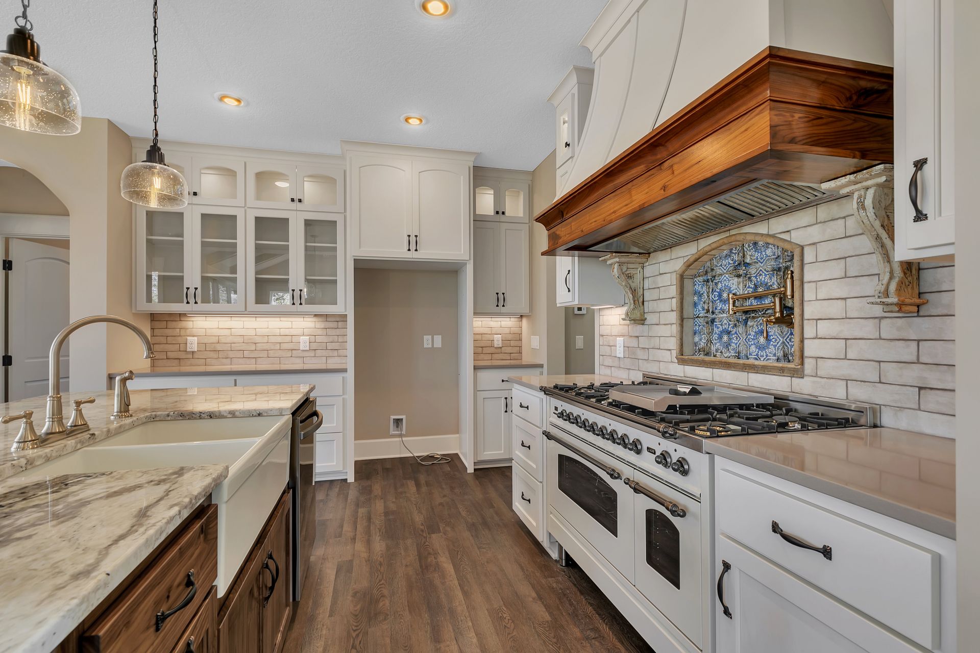 A kitchen with white cabinets , a stove , a sink , and a wooden hood.