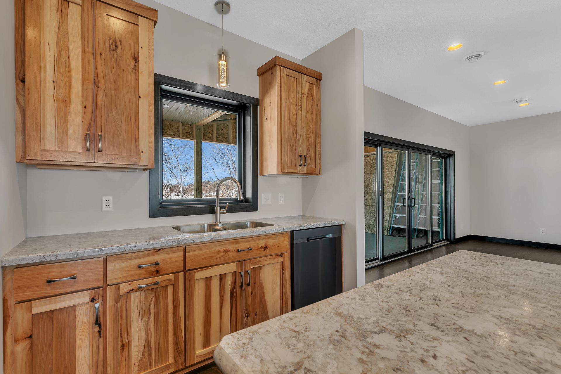 A kitchen with wooden cabinets , granite counter tops , a sink and a window.