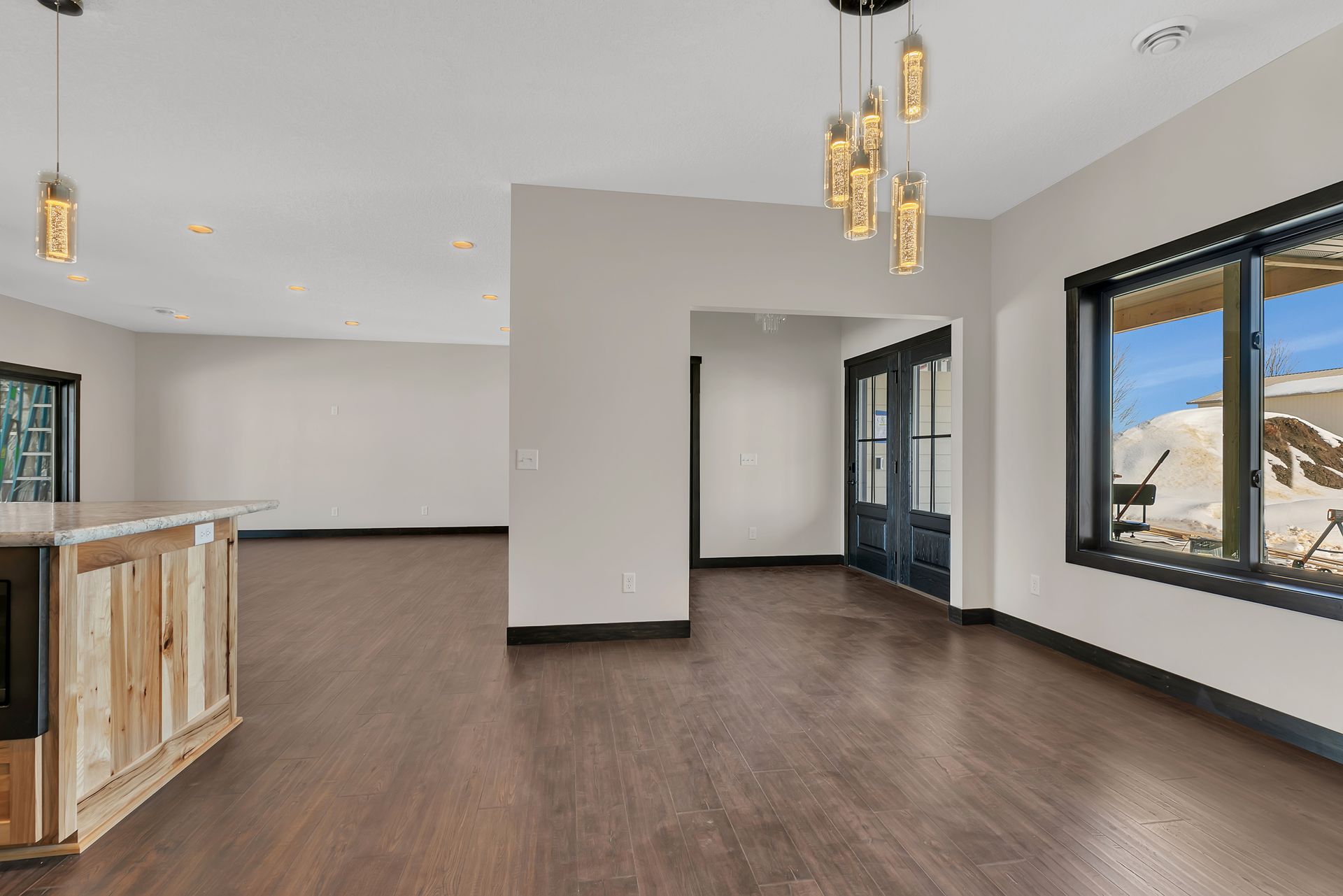 An empty living room with hardwood floors , a bar , and a lot of windows.