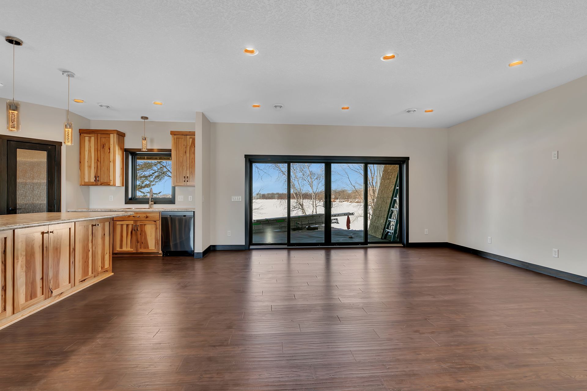 A large empty room with hardwood floors and sliding glass doors leading to a kitchen.