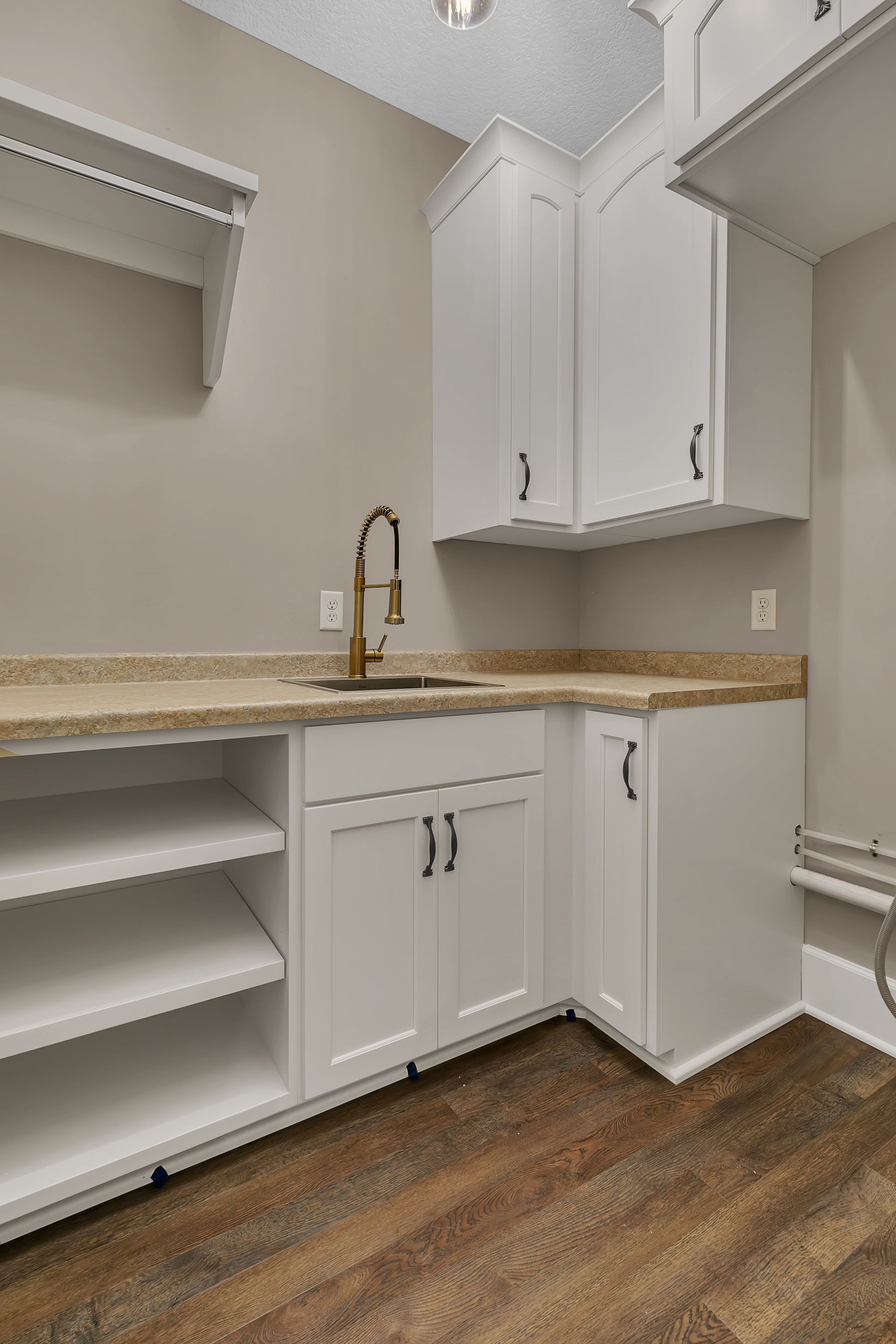 A laundry room with white cabinets , a sink , and wooden floors.