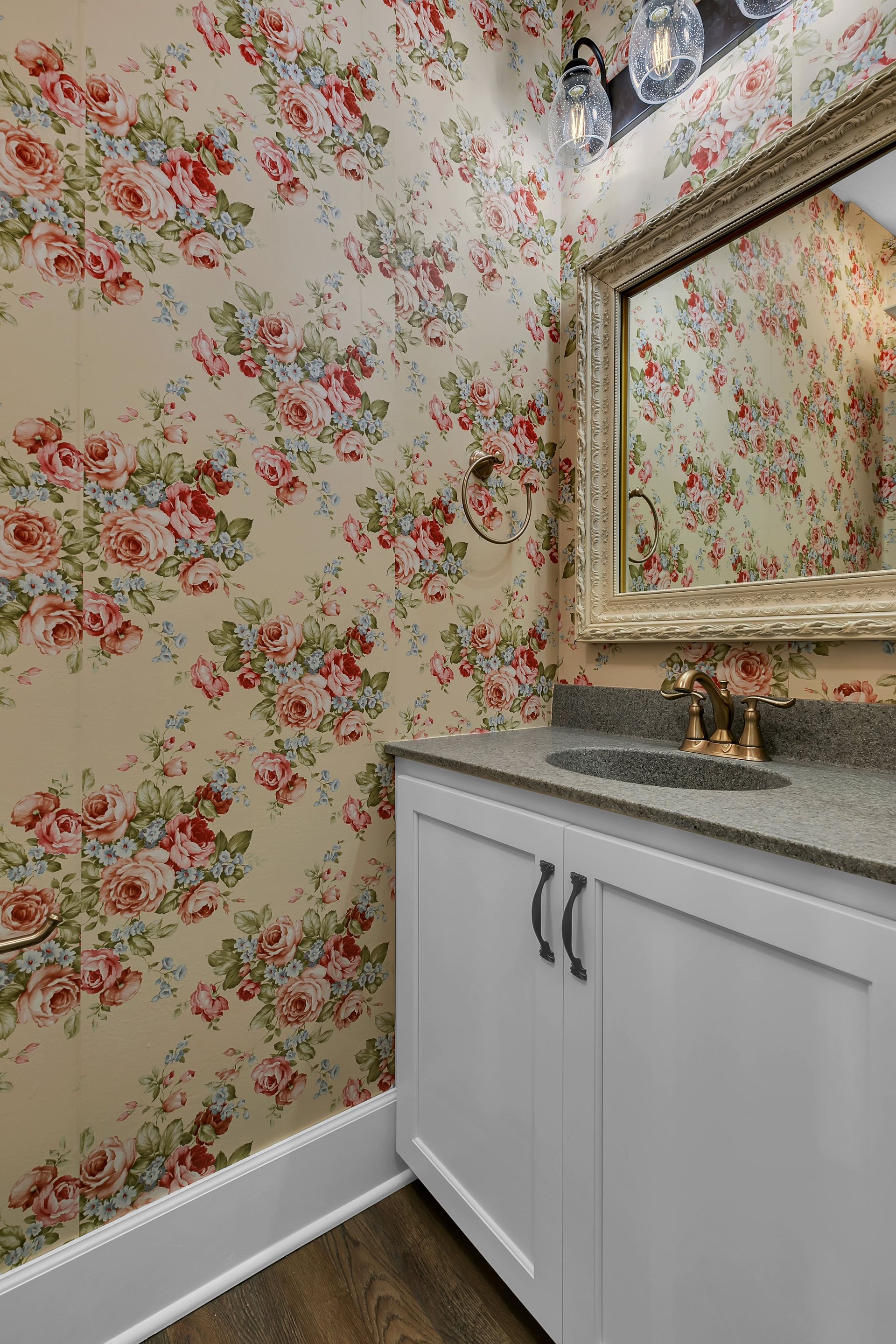 A bathroom with a sink , mirror and floral wallpaper.