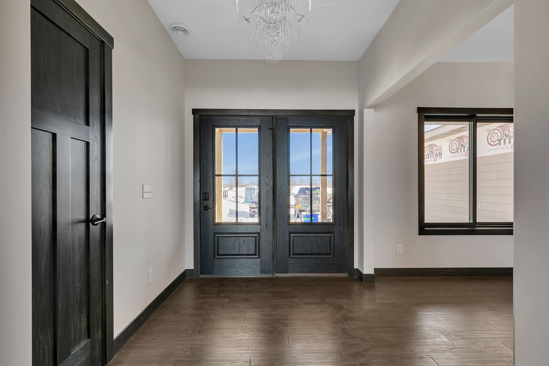 An empty room with a black door and two windows.