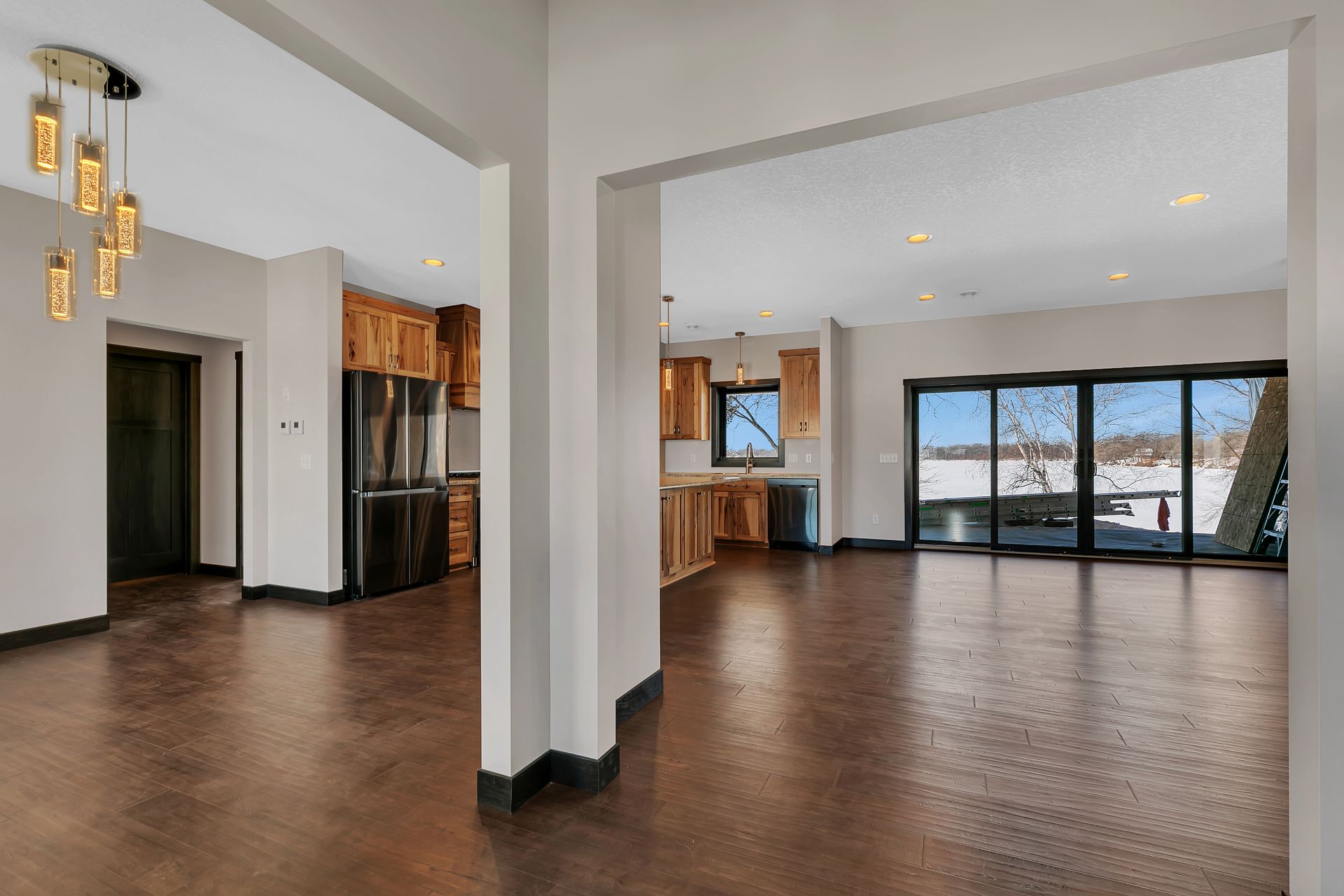 A large empty room with hardwood floors and sliding glass doors leading to a kitchen.