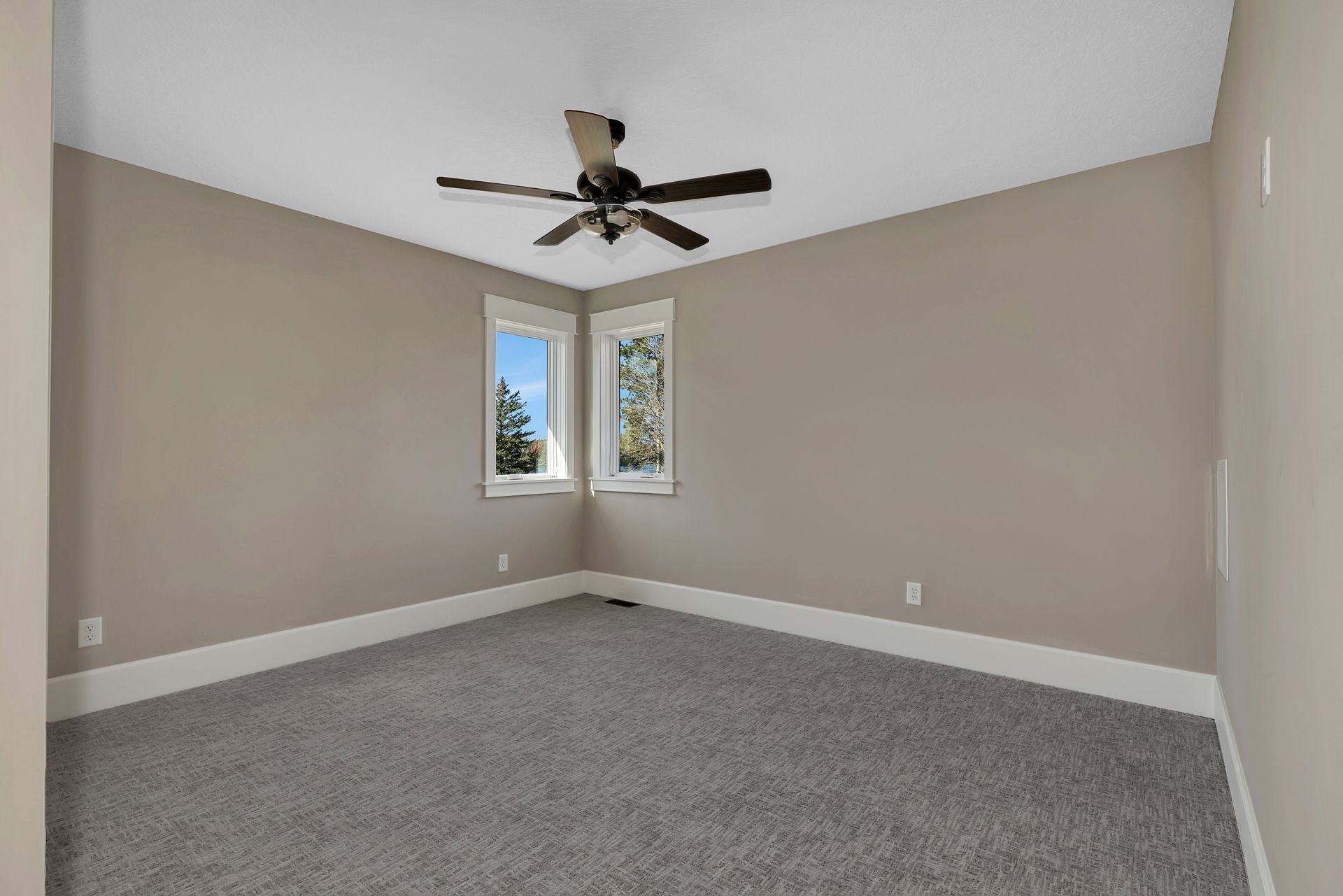 An empty bedroom with a ceiling fan and two windows.