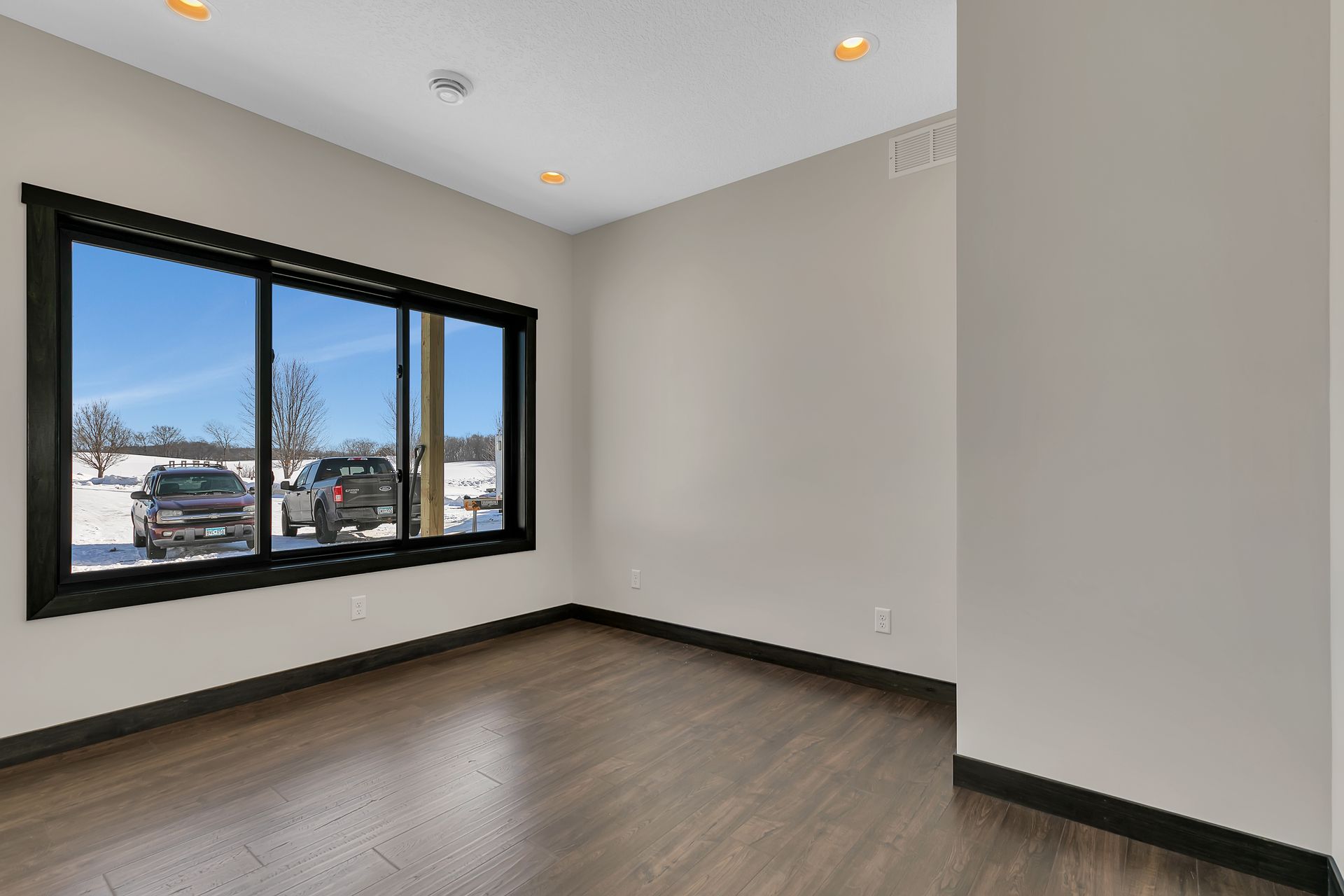 An empty room with a large window and a view of a parking lot.