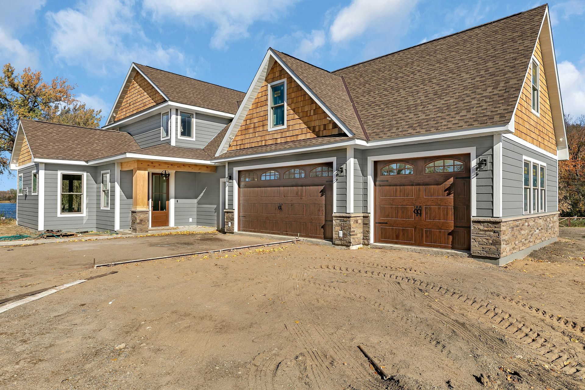 New suburban house exterior with double wooden garage doors and unfinished front yard