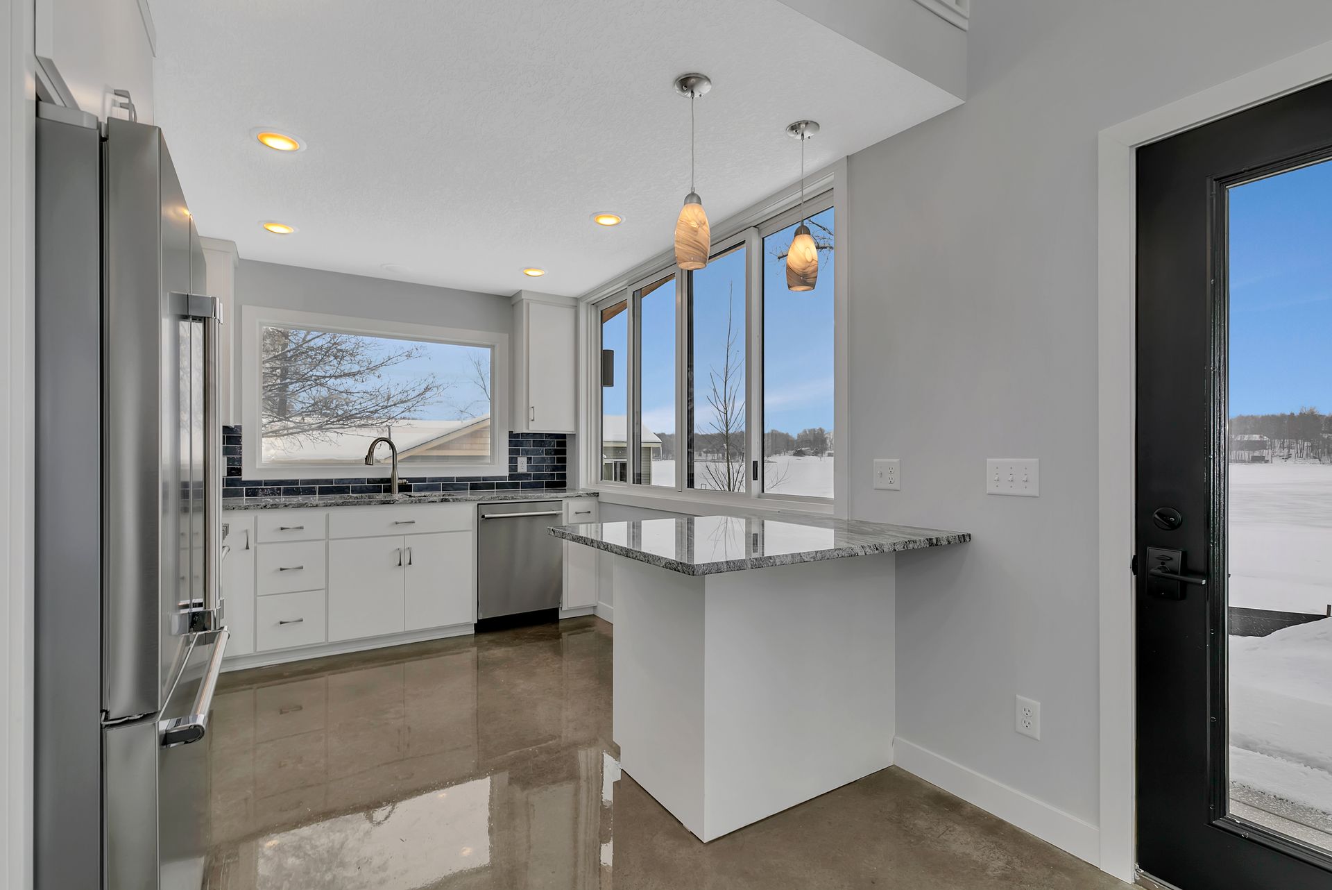 A kitchen with white cabinets , stainless steel appliances , granite counter tops and a large island.