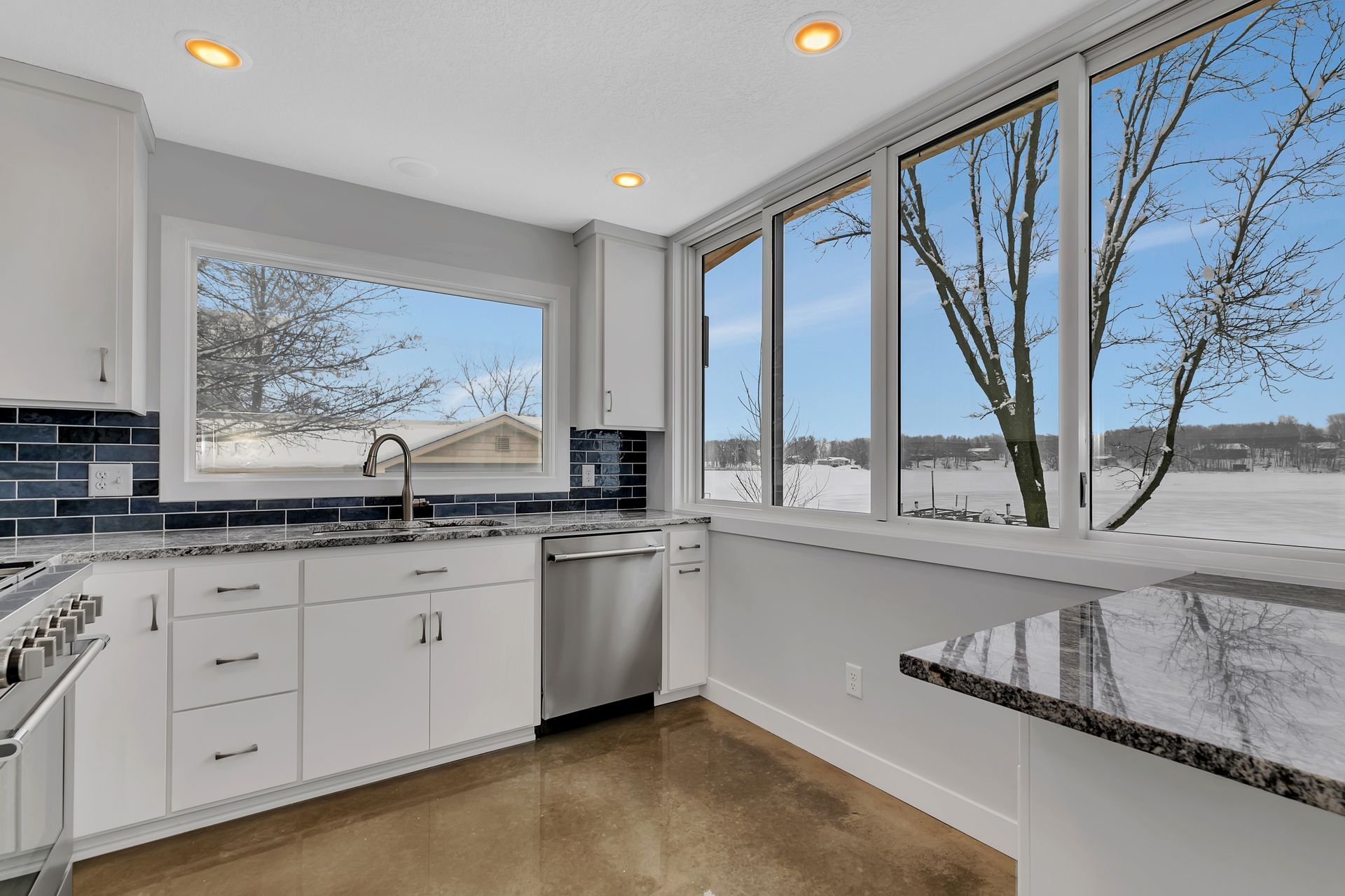 A kitchen with white cabinets , granite counter tops , stainless steel appliances and a large window.