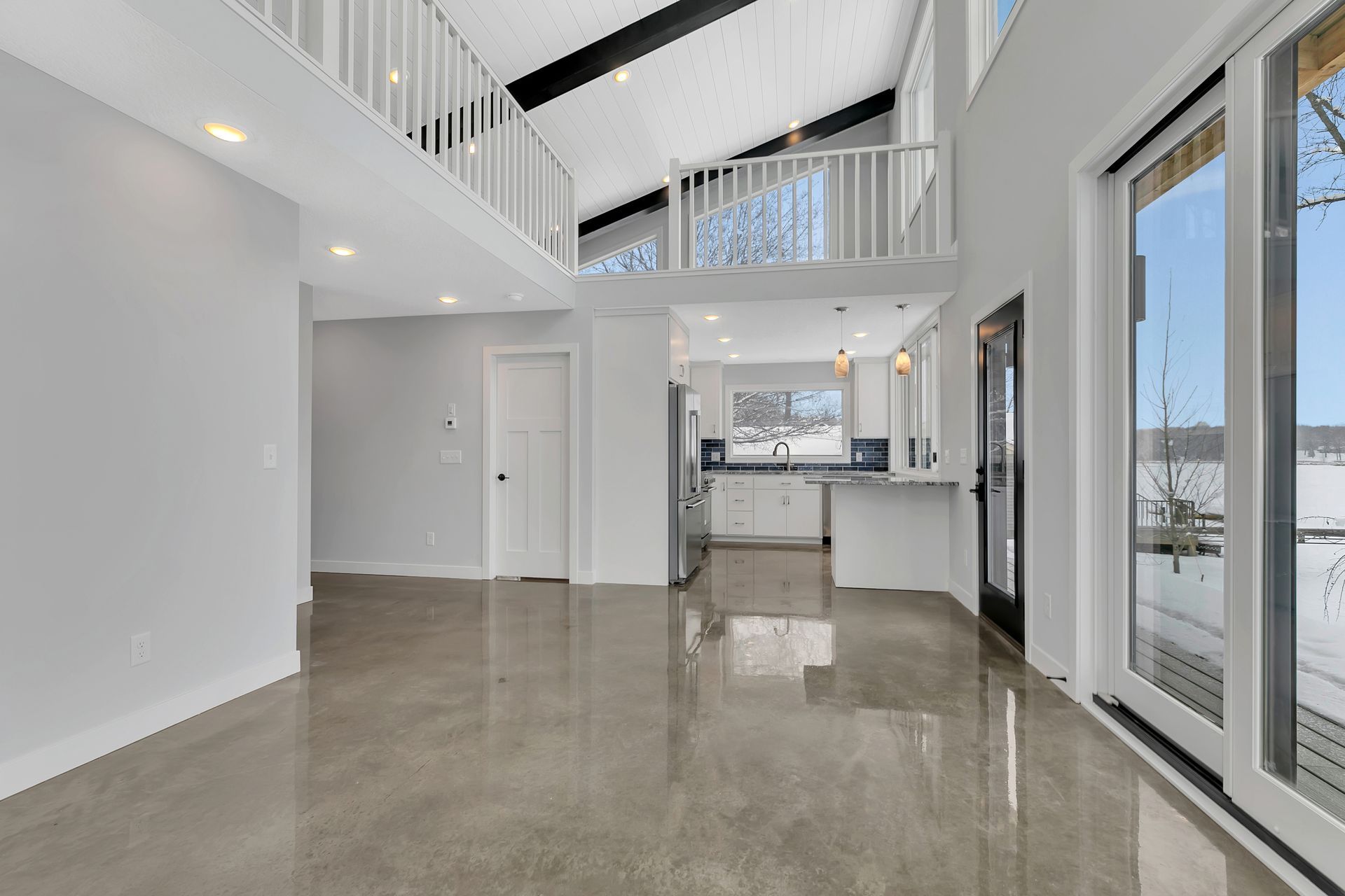 A large empty room with a kitchen and sliding glass doors.