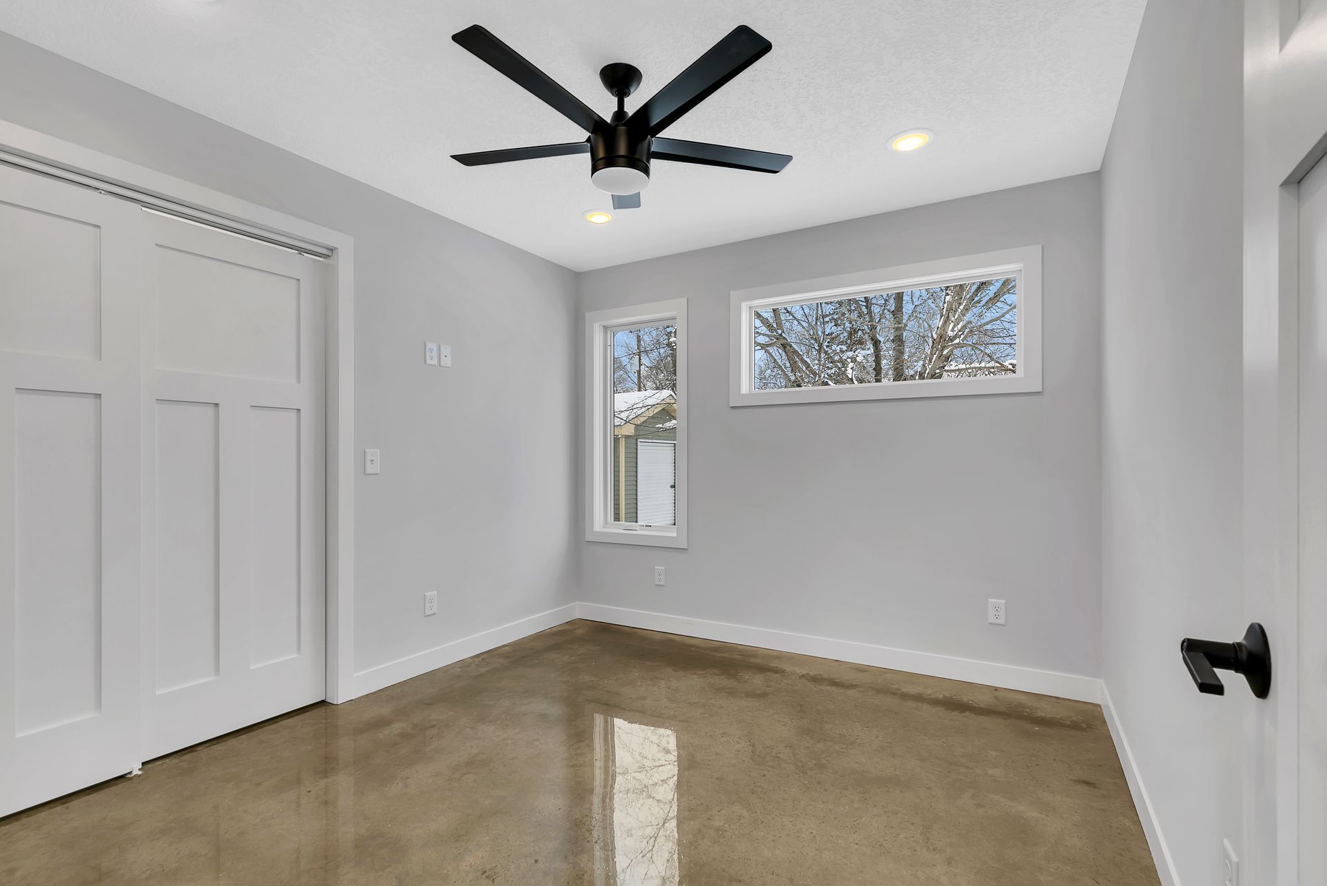 An empty room with a ceiling fan and two windows.