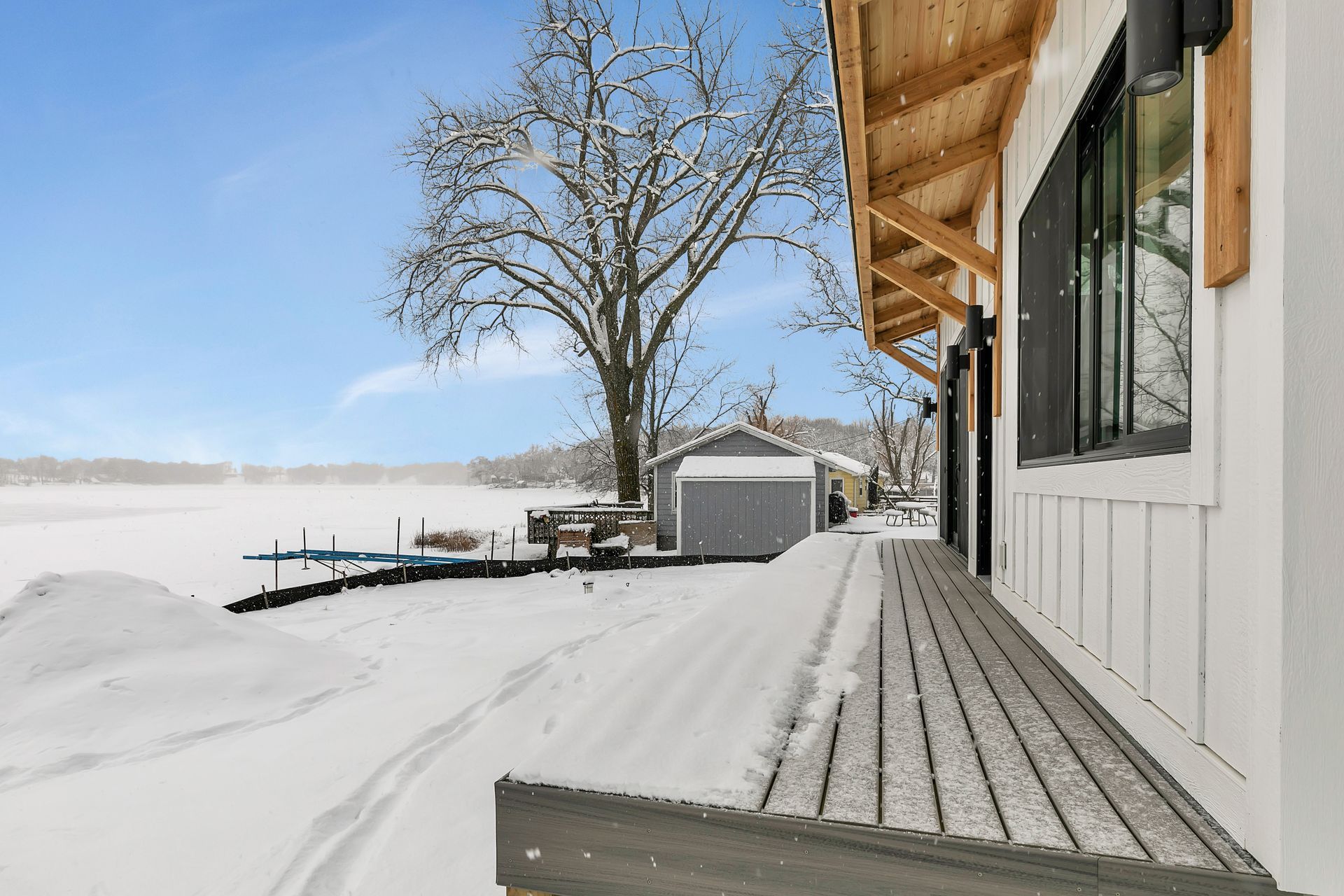 A house with a porch covered in snow and a shed in the background.