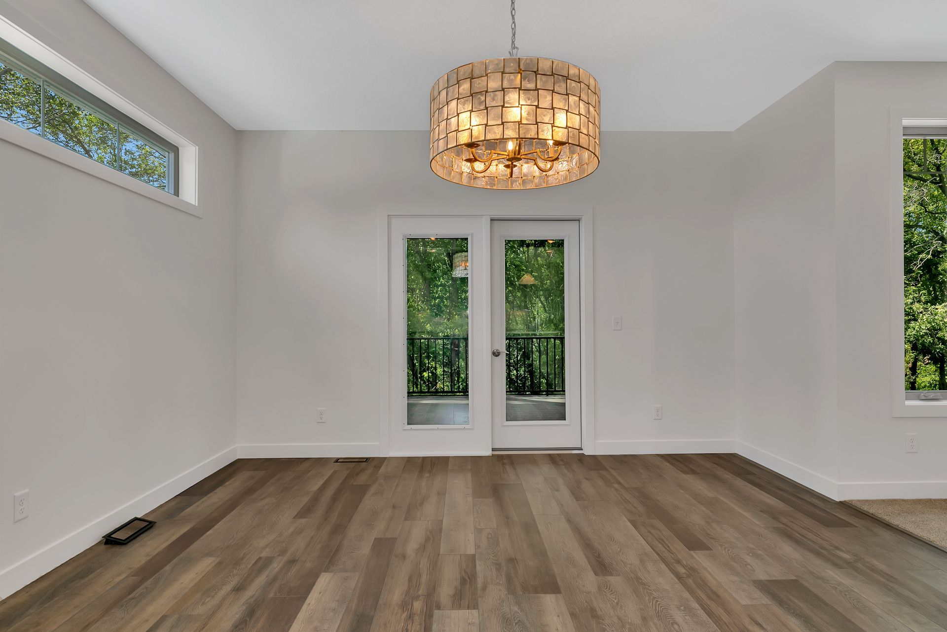 An empty room with hardwood floors and a chandelier hanging from the ceiling.