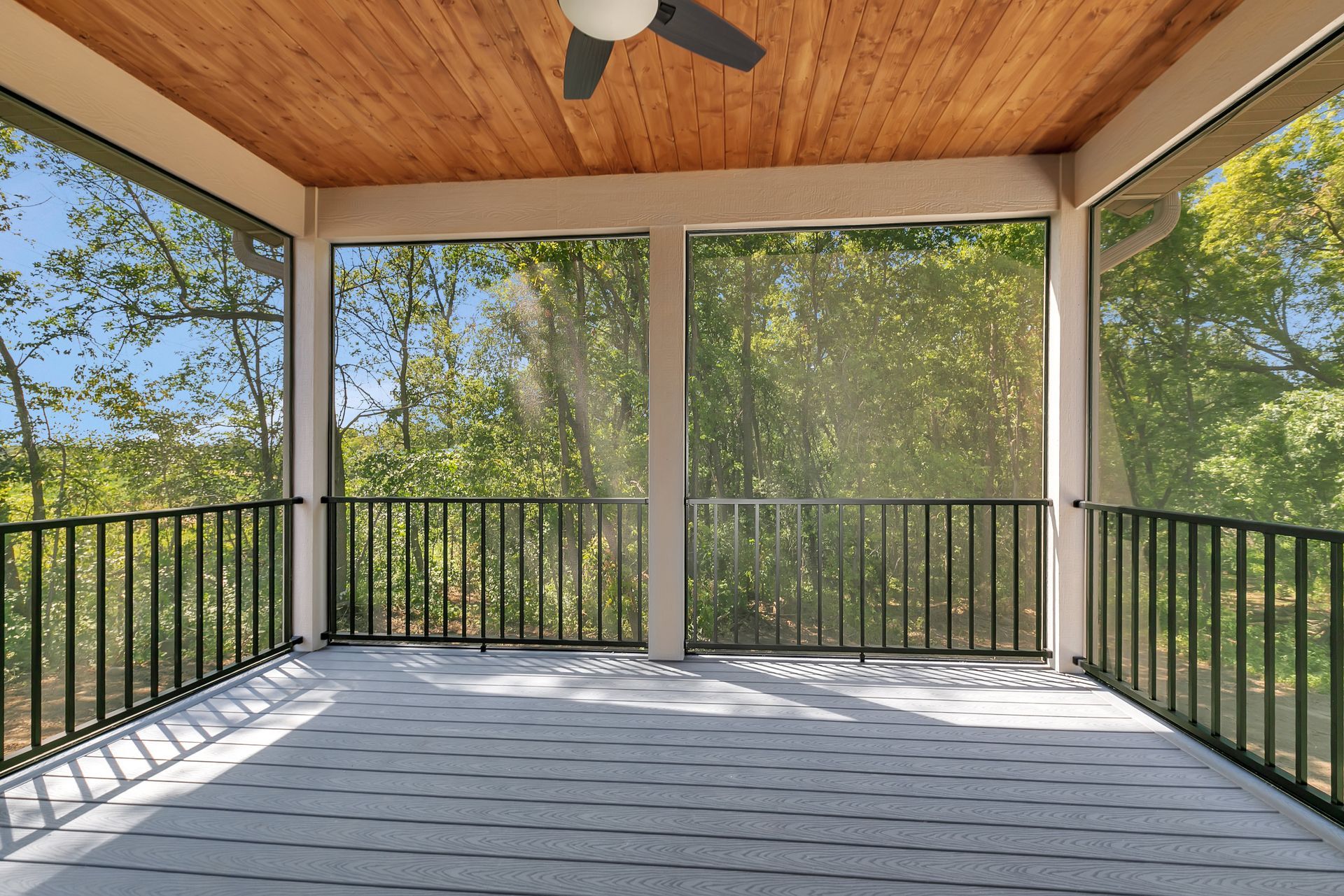 An empty screened in porch with a ceiling fan