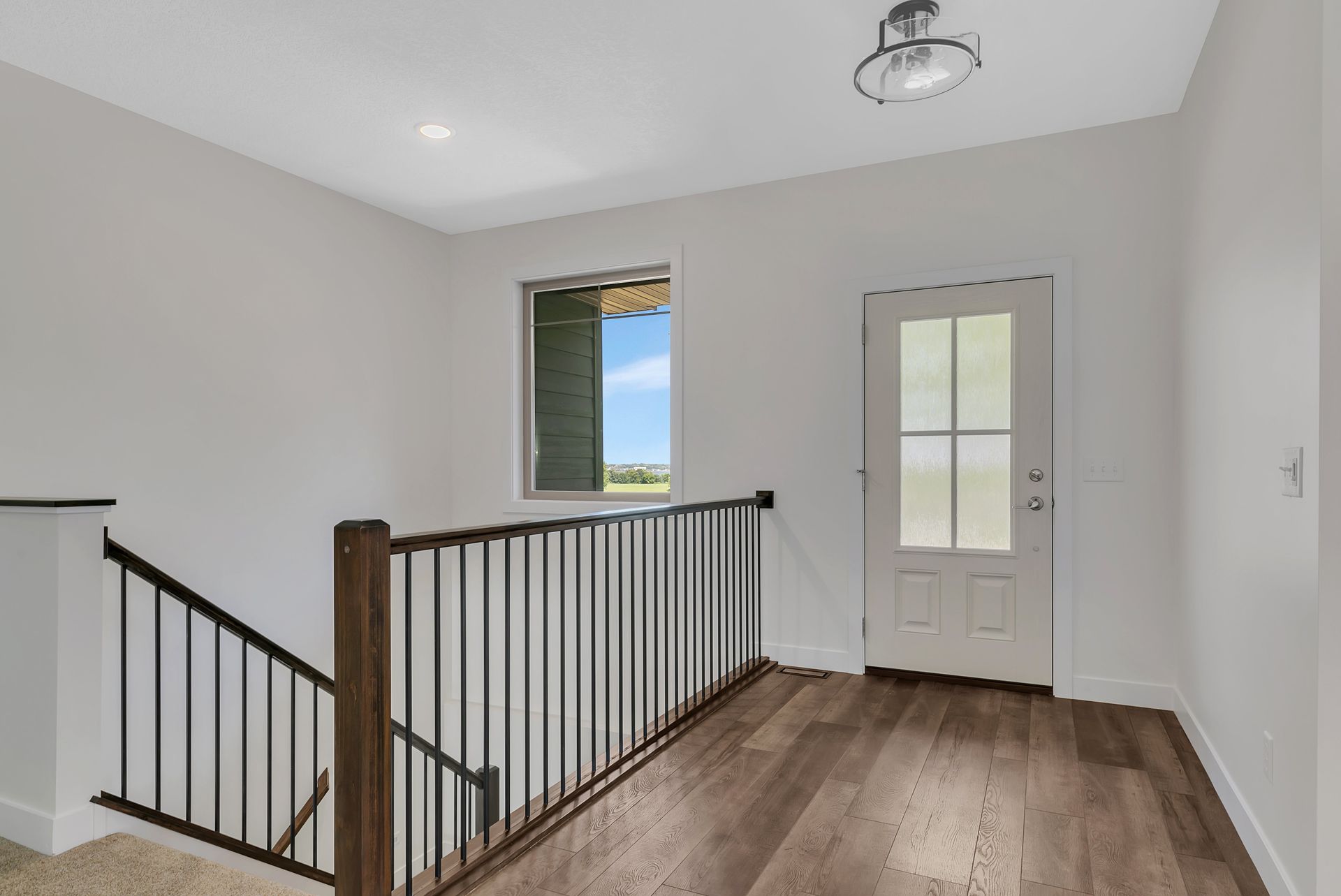 A hallway with stairs leading up to a door and a window.