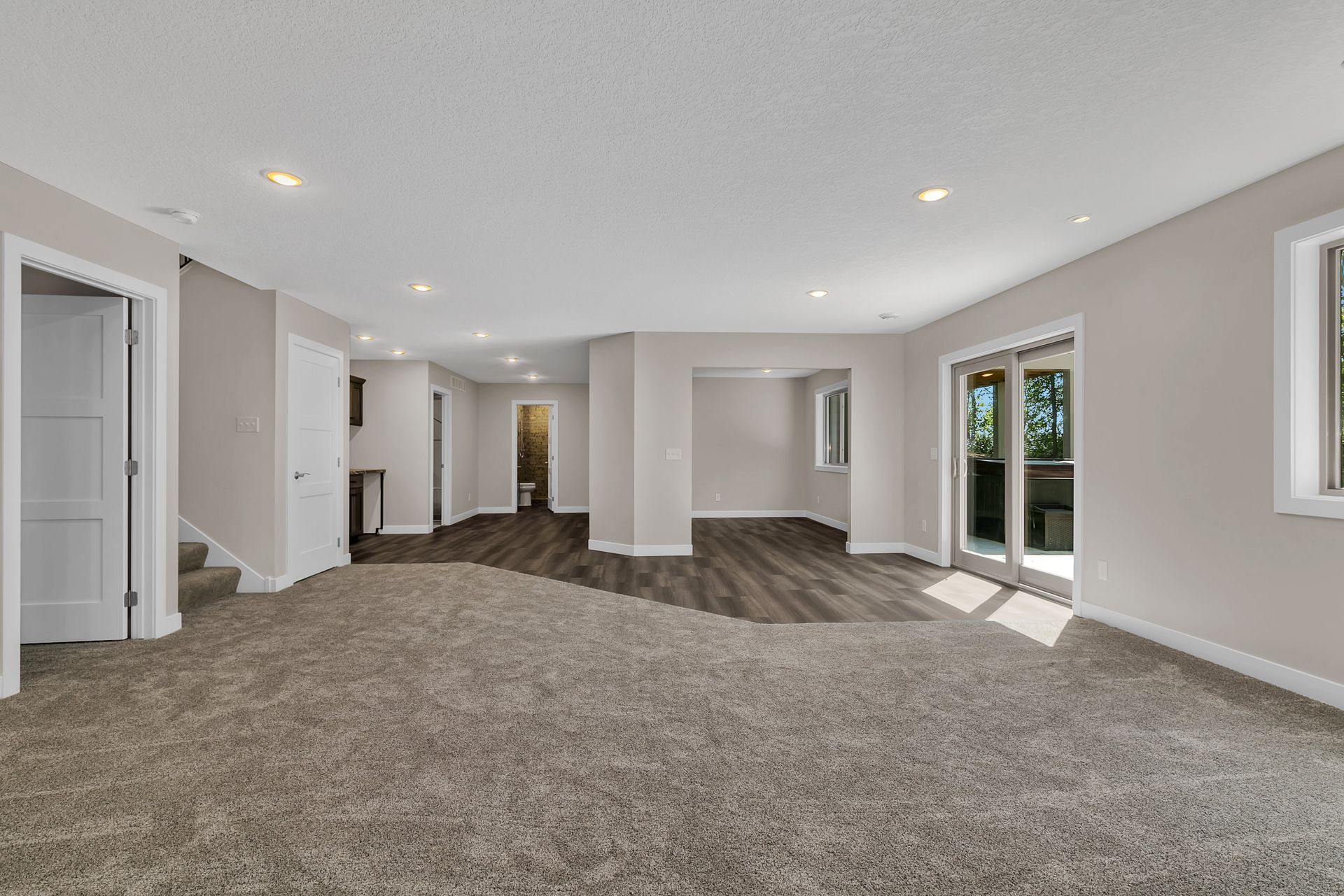 An empty basement with a carpeted floor and sliding glass doors.