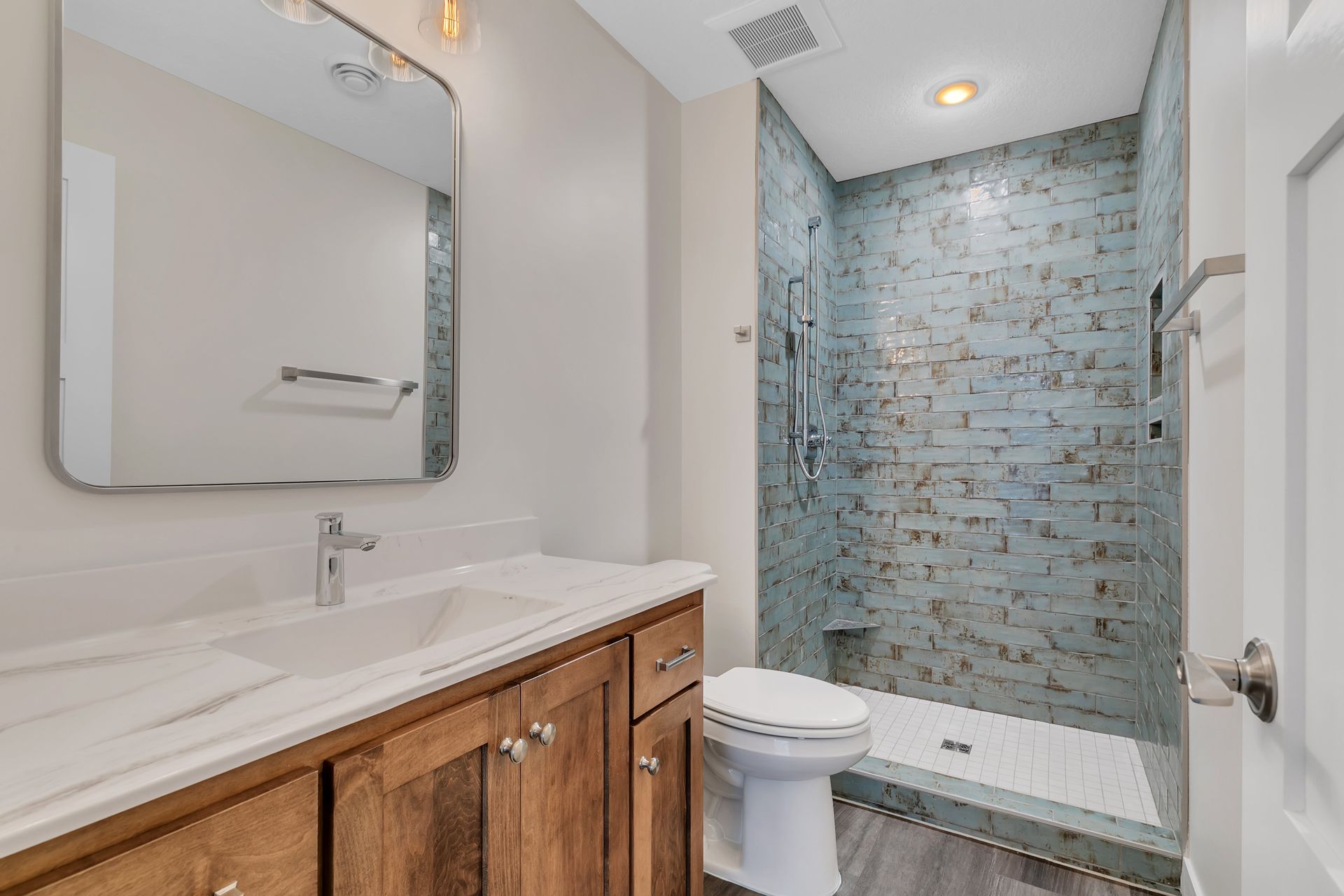 A bathroom with a toilet , sink , mirror and walk in shower.