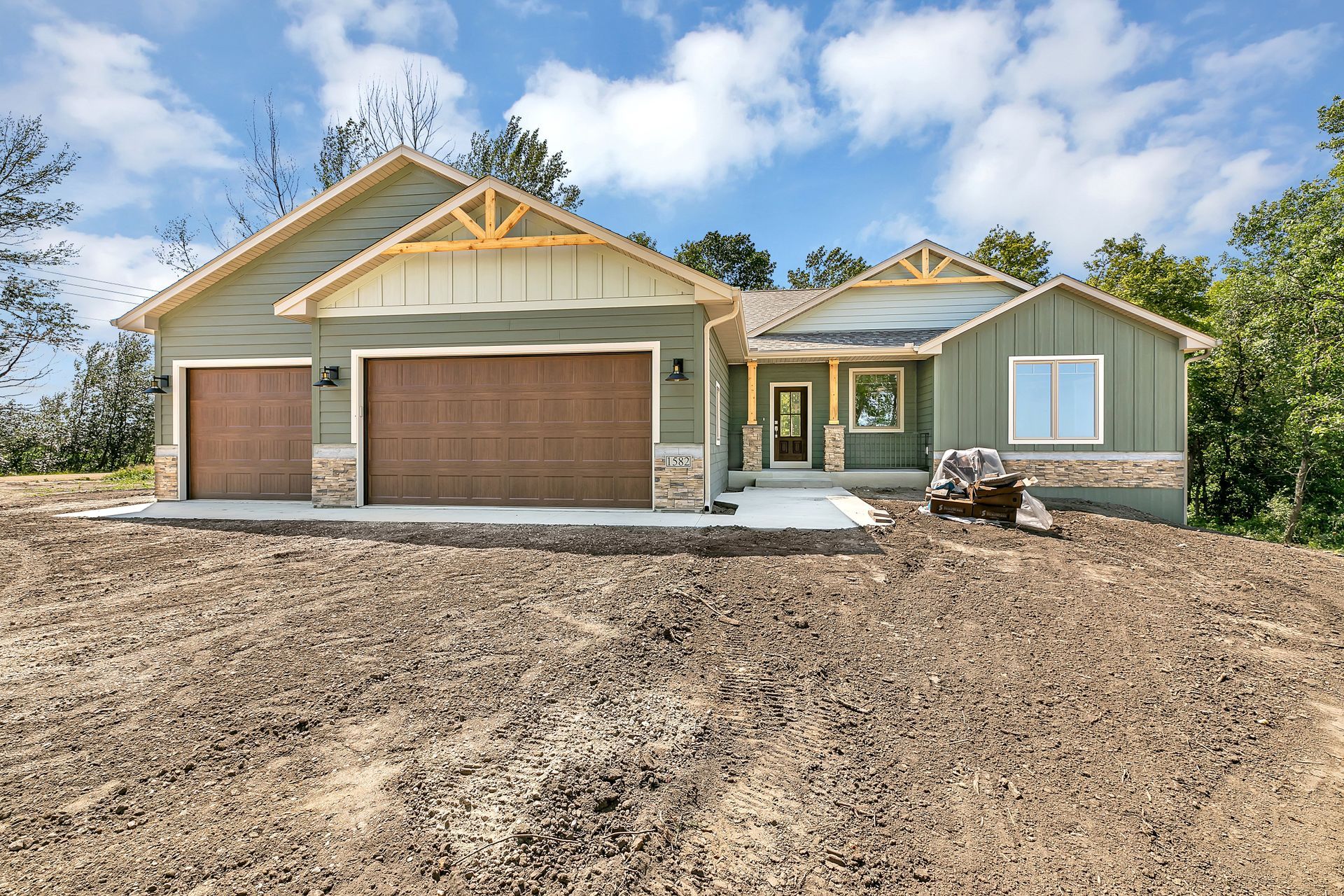 A green house with a brown garage door is sitting on top of a dirt hill.