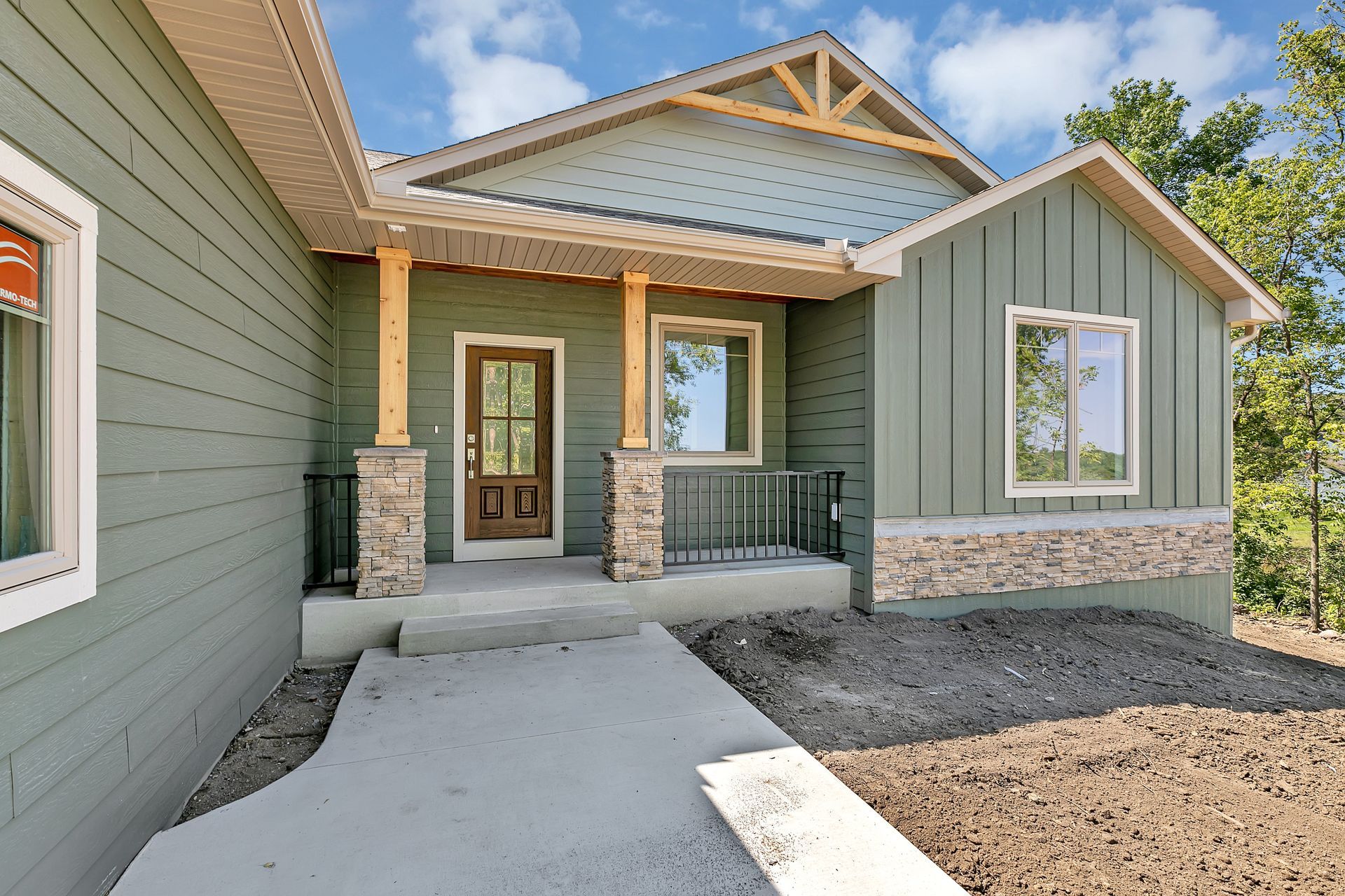 A green house with a porch and a concrete walkway