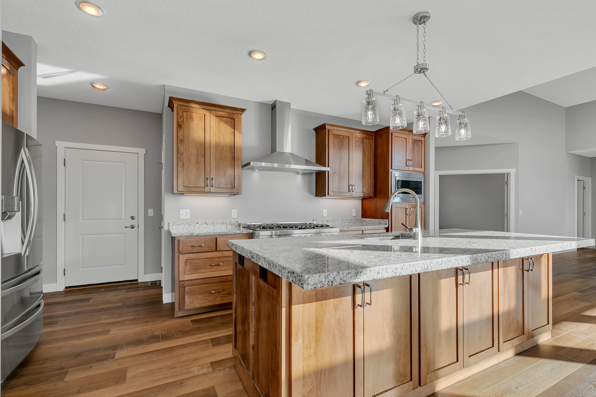 A kitchen with wooden cabinets , granite counter tops , stainless steel appliances and a large island.