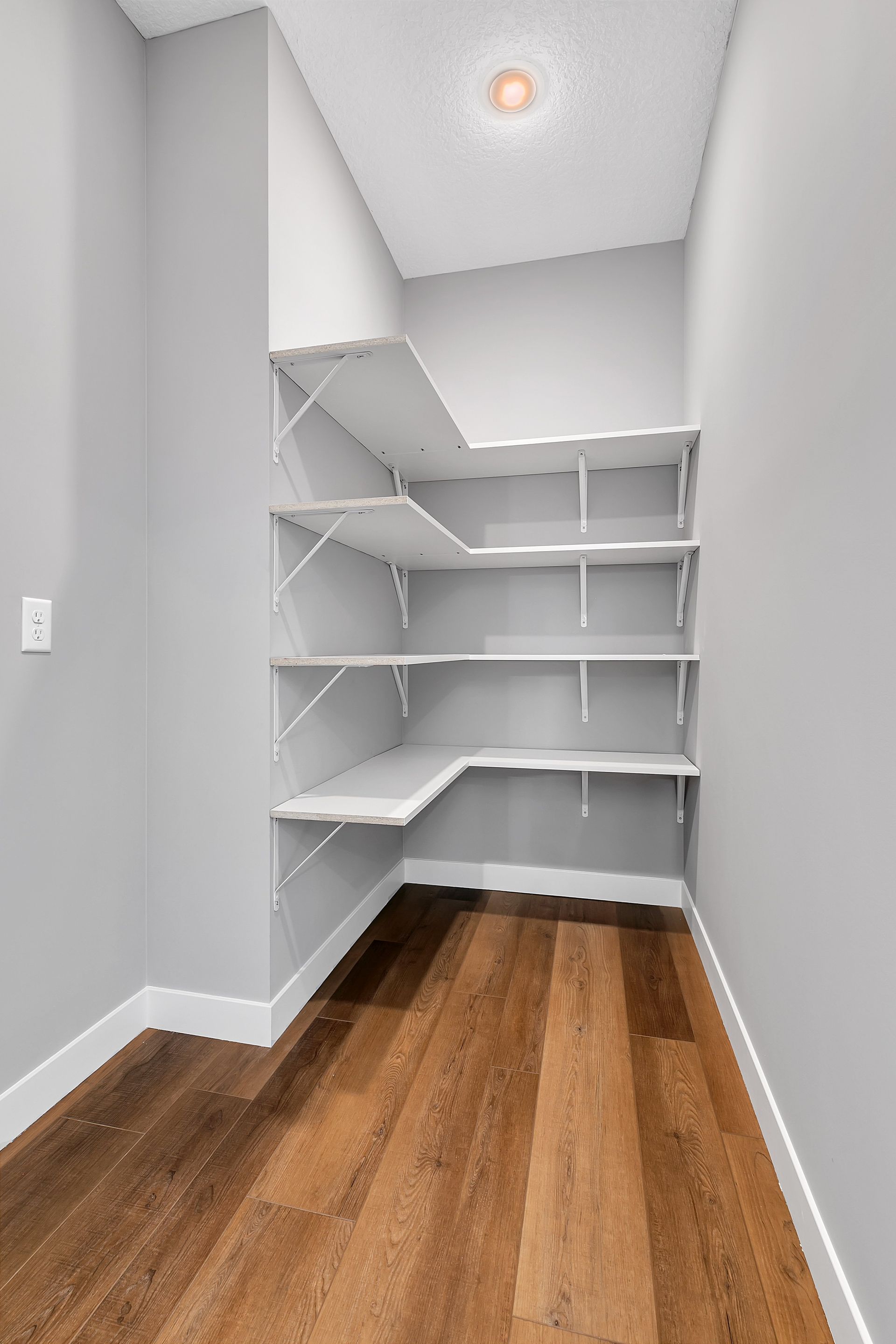 An empty walk in closet with hardwood floors and white shelves.