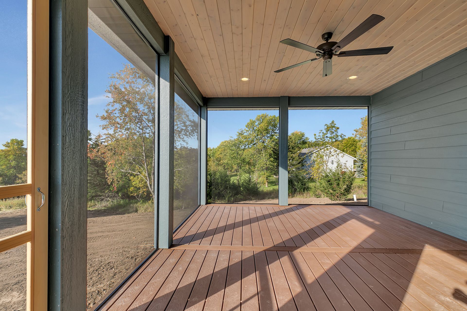 A screened in porch with a wooden deck and a ceiling fan.