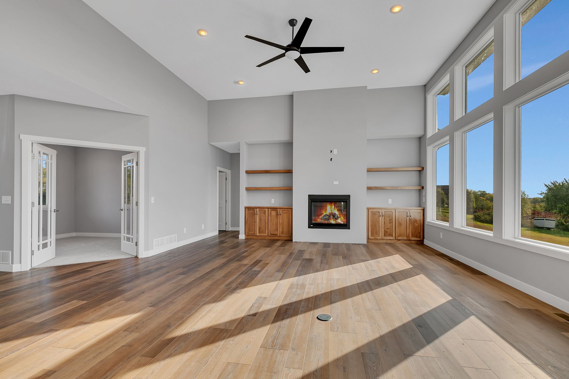 An empty living room with hardwood floors , a fireplace and a ceiling fan.