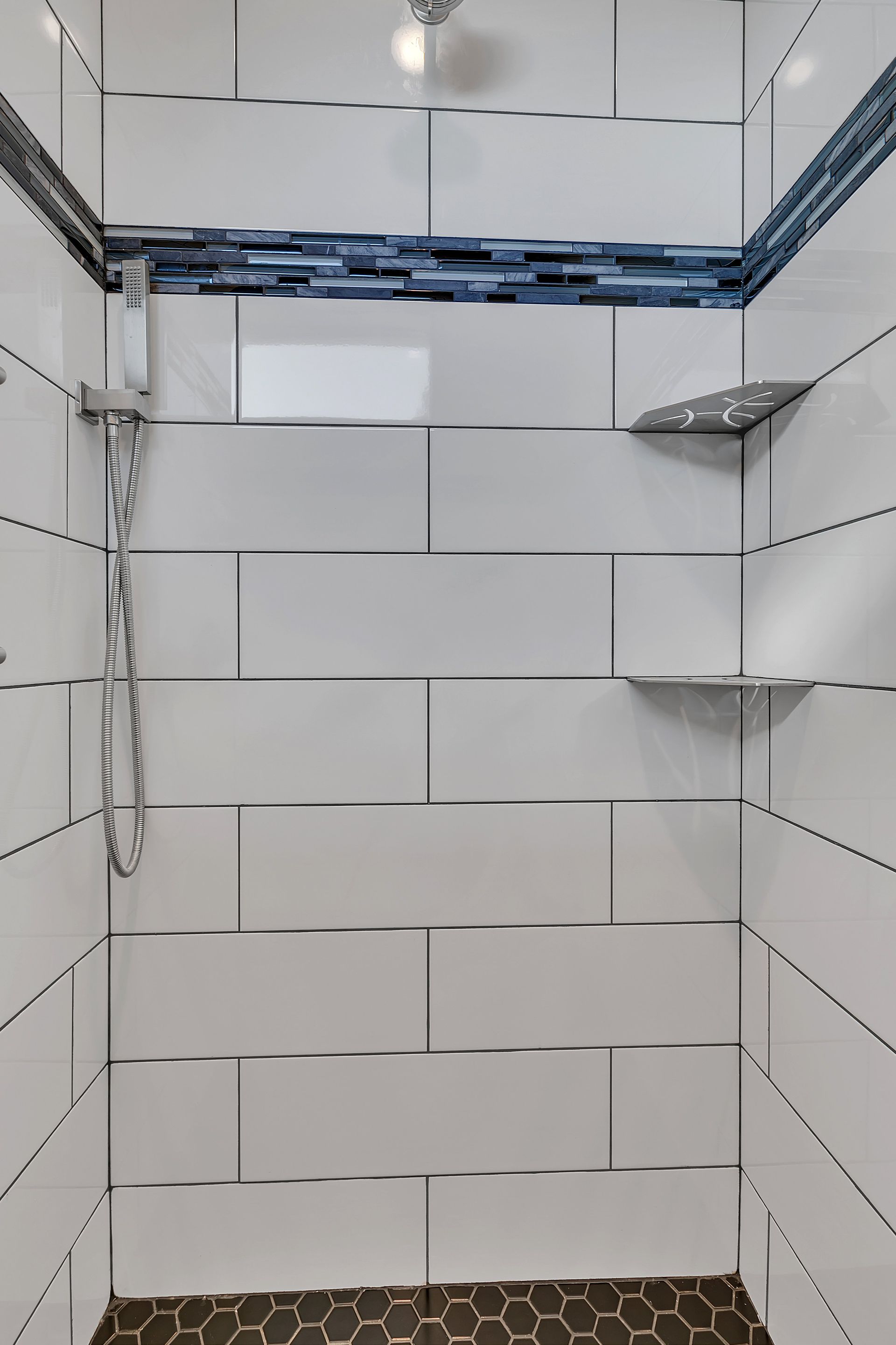 A bathroom with white tiles and a walk in shower with a glass door.