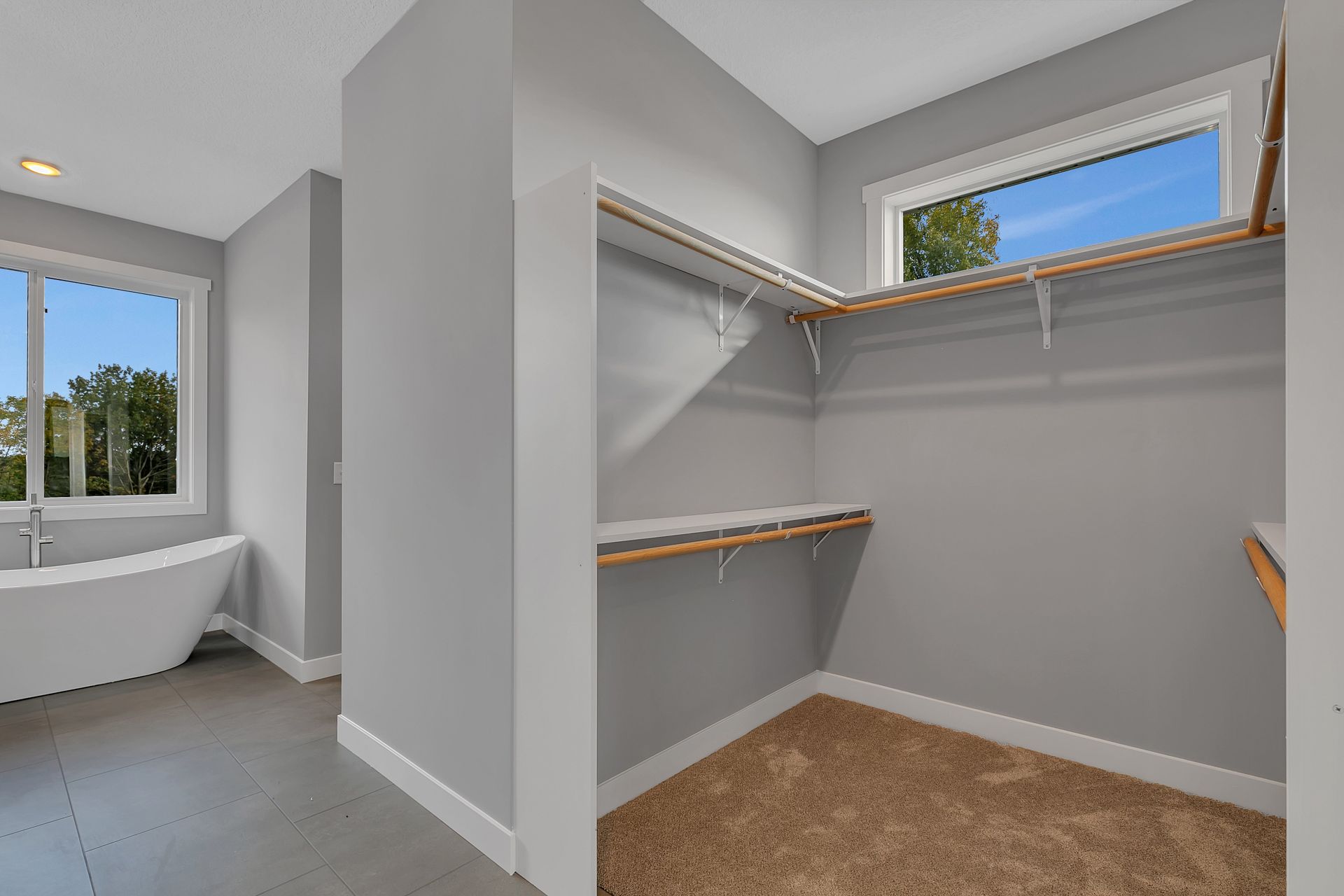 A walk in closet in a bathroom with a tub and a window.