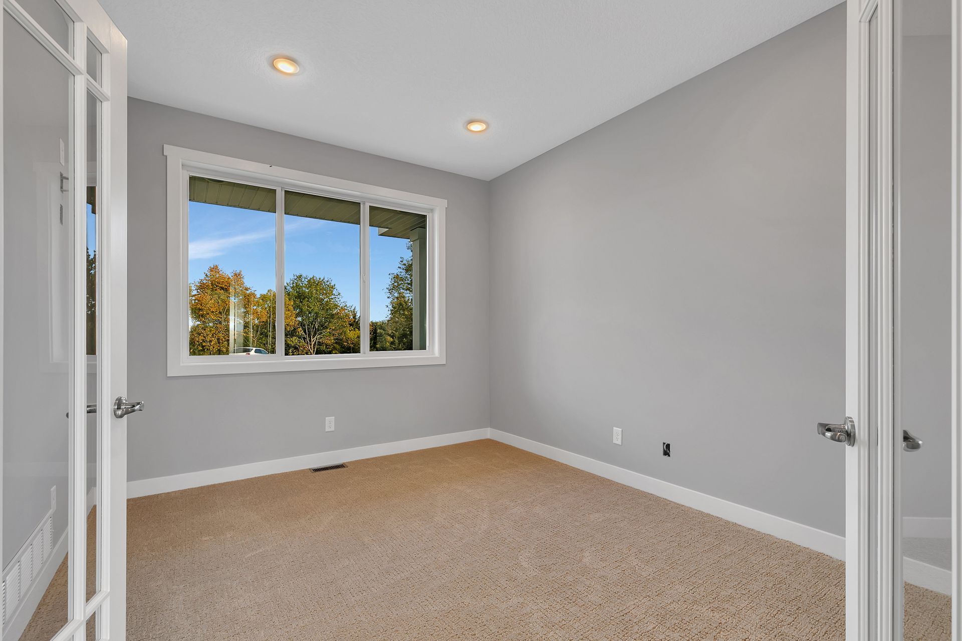 An empty bedroom with a large window and a carpeted floor.