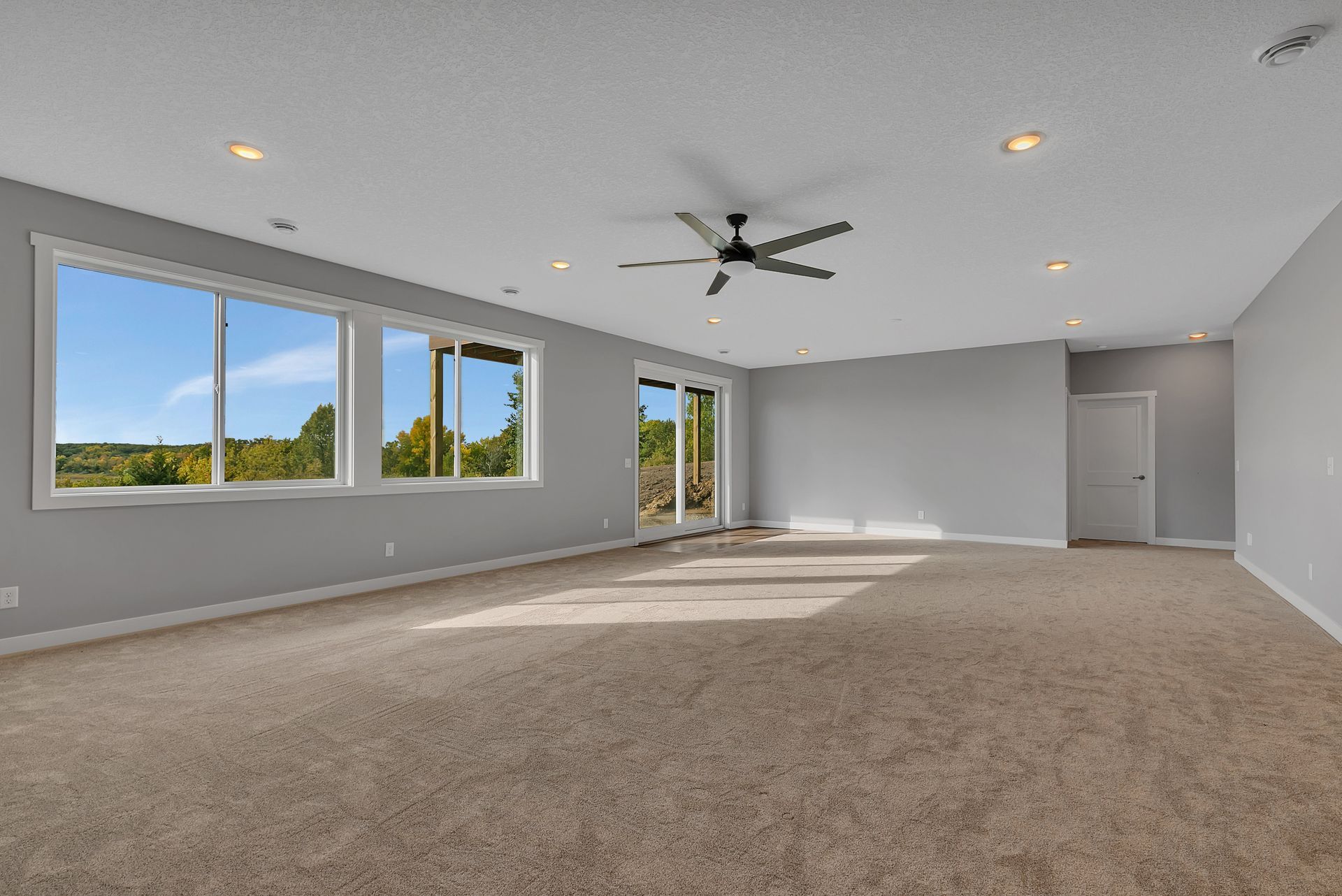 A large empty room with a ceiling fan and a lot of windows.
