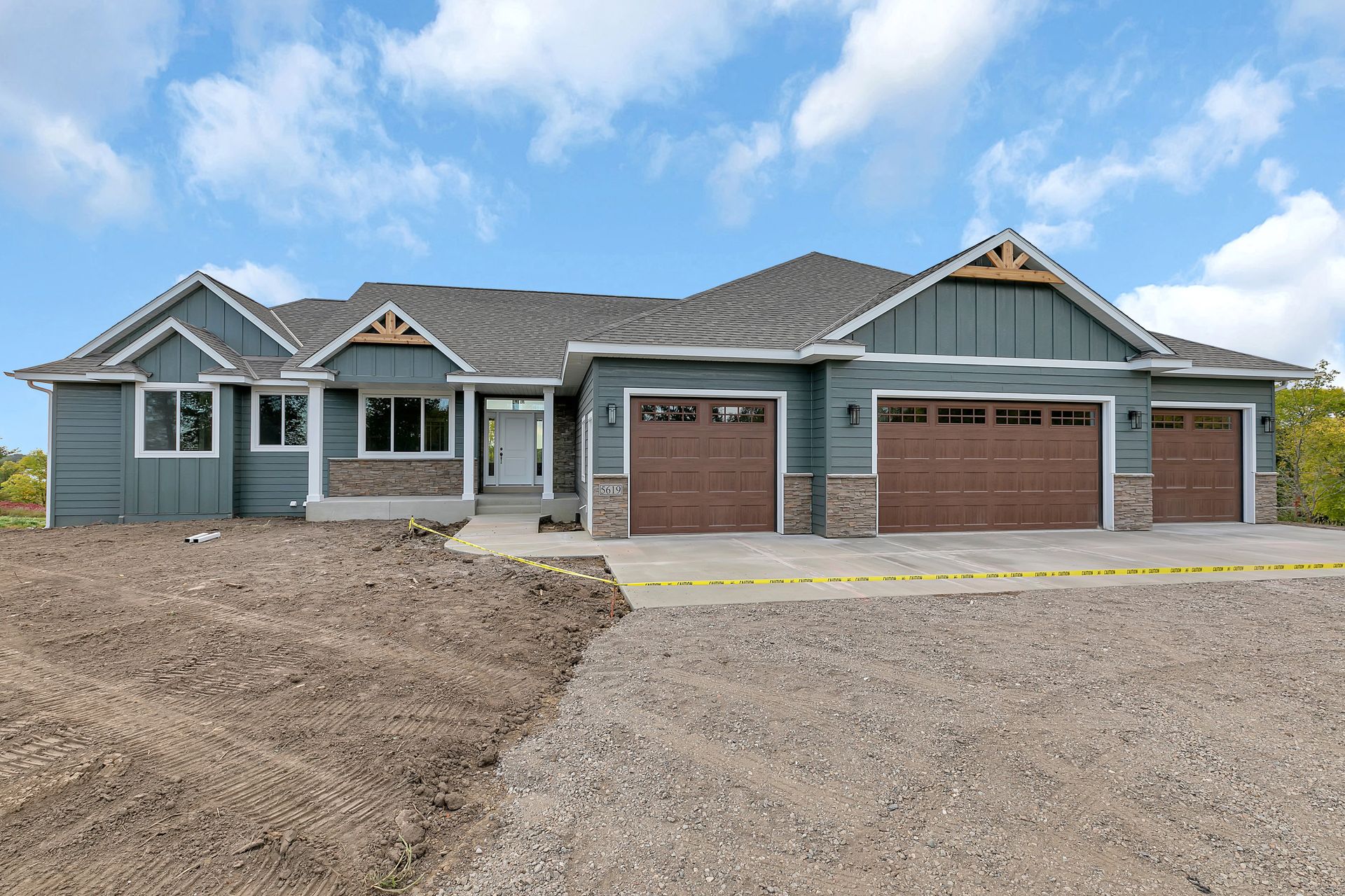 A large house with three garage doors is sitting on top of a dirt field.
