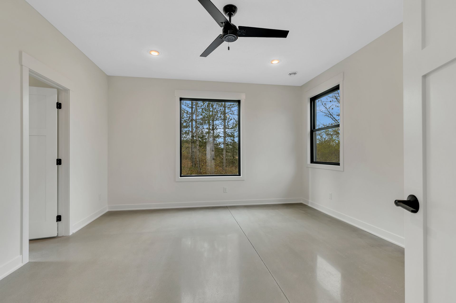 An empty room with a ceiling fan and two windows.