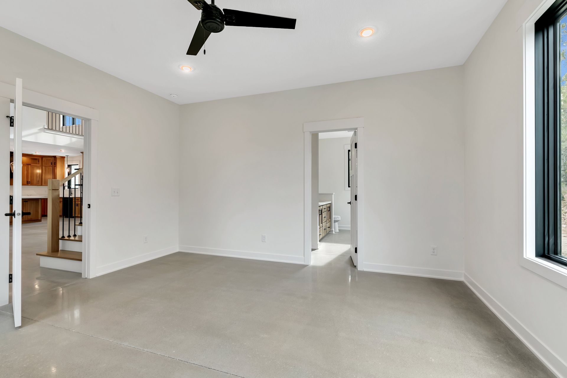 An empty room with a ceiling fan and two windows.