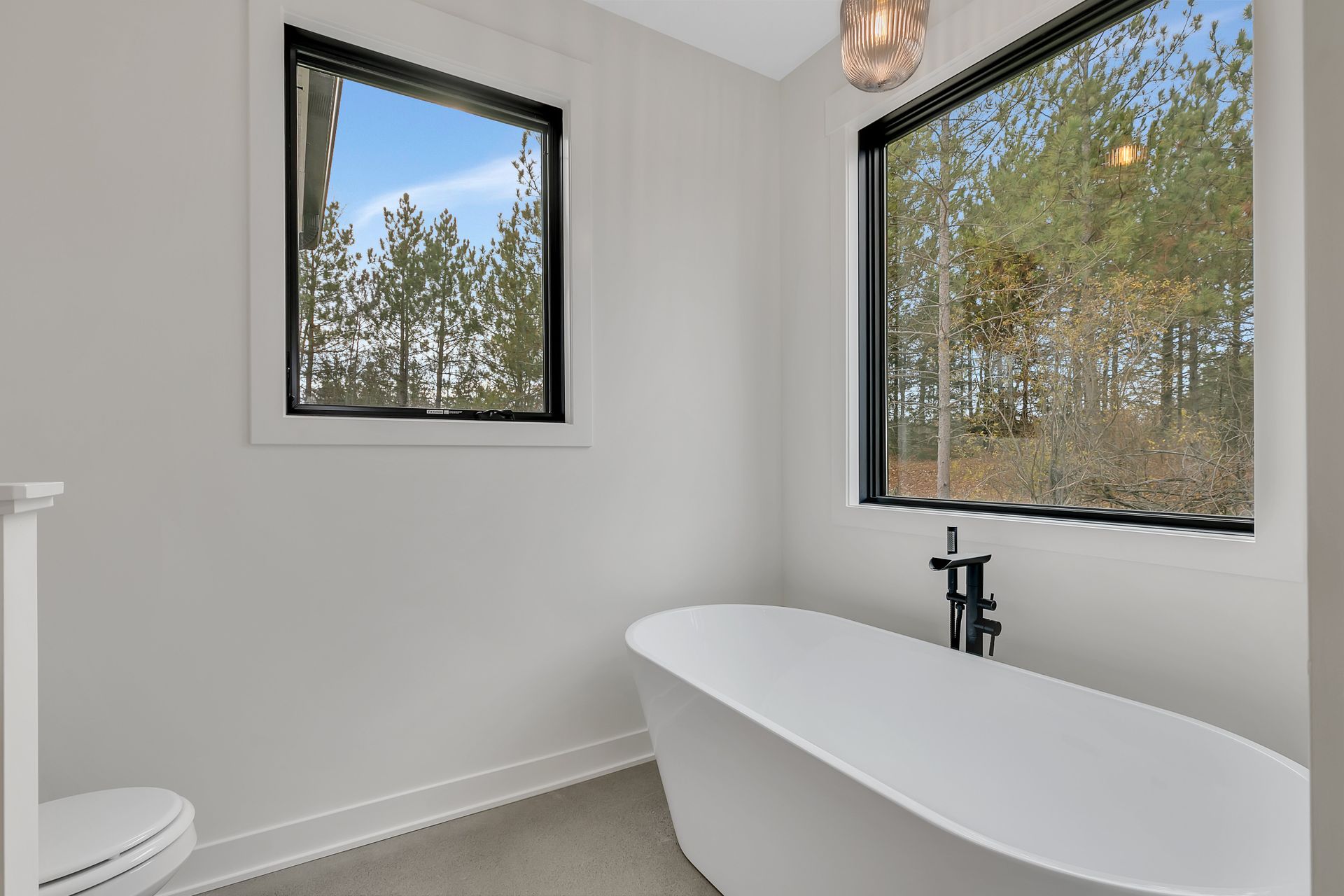A bathroom with a tub , toilet , and two windows.