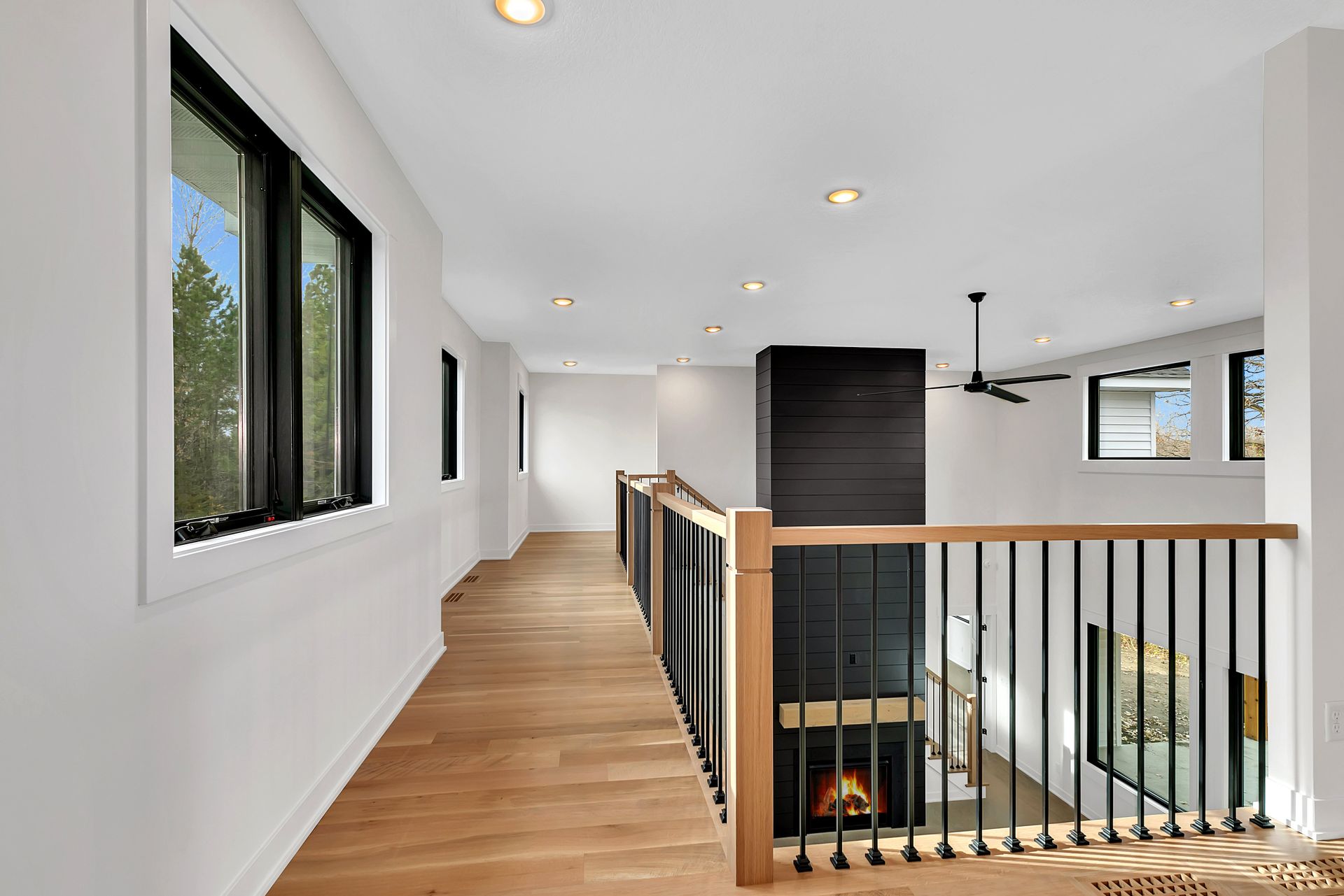A long hallway in a house with a wooden floor and a black railing.