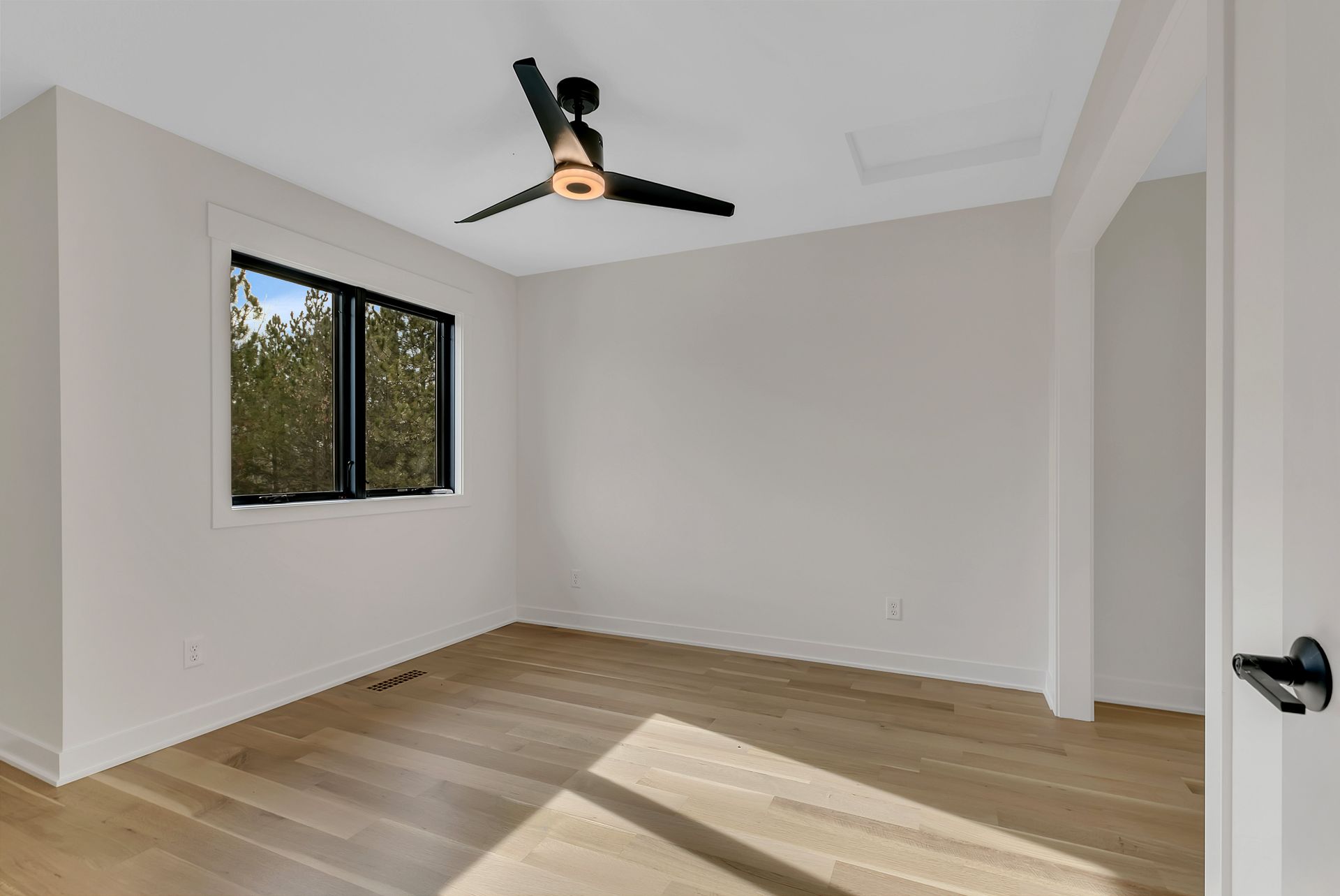 An empty room with a ceiling fan and two windows.