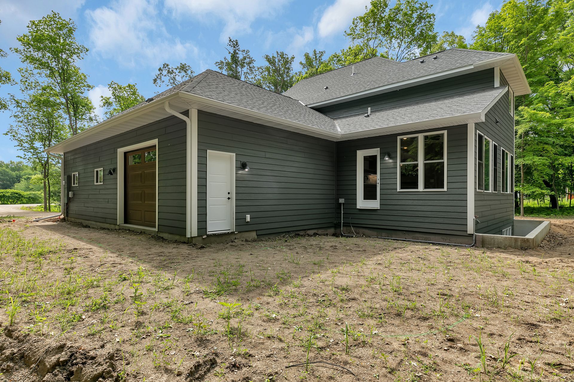 A gray house with a garage and a lot of windows is sitting on top of a dirt field.