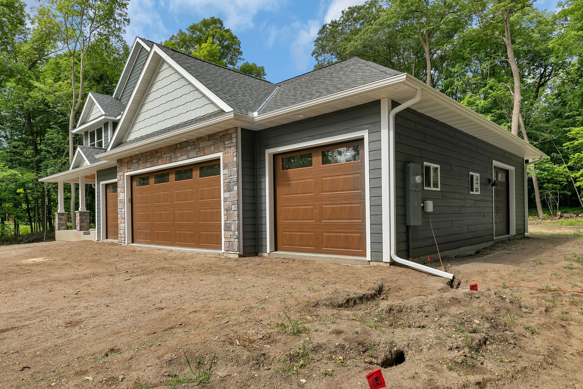 A large house with three garage doors is sitting on top of a dirt field.