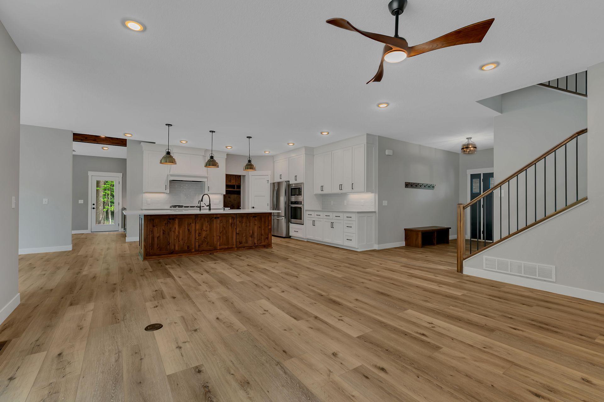 A kitchen and living room in a house with hardwood floors and a ceiling fan.