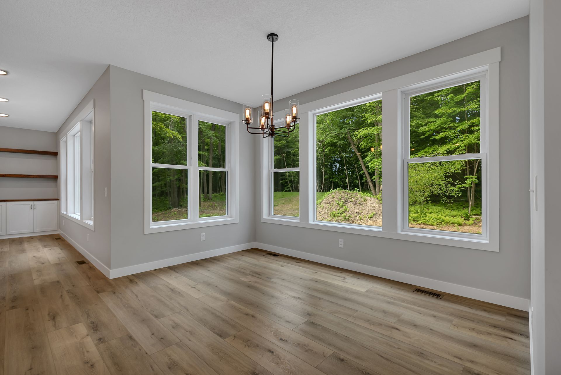 An empty living room with hardwood floors and lots of windows.