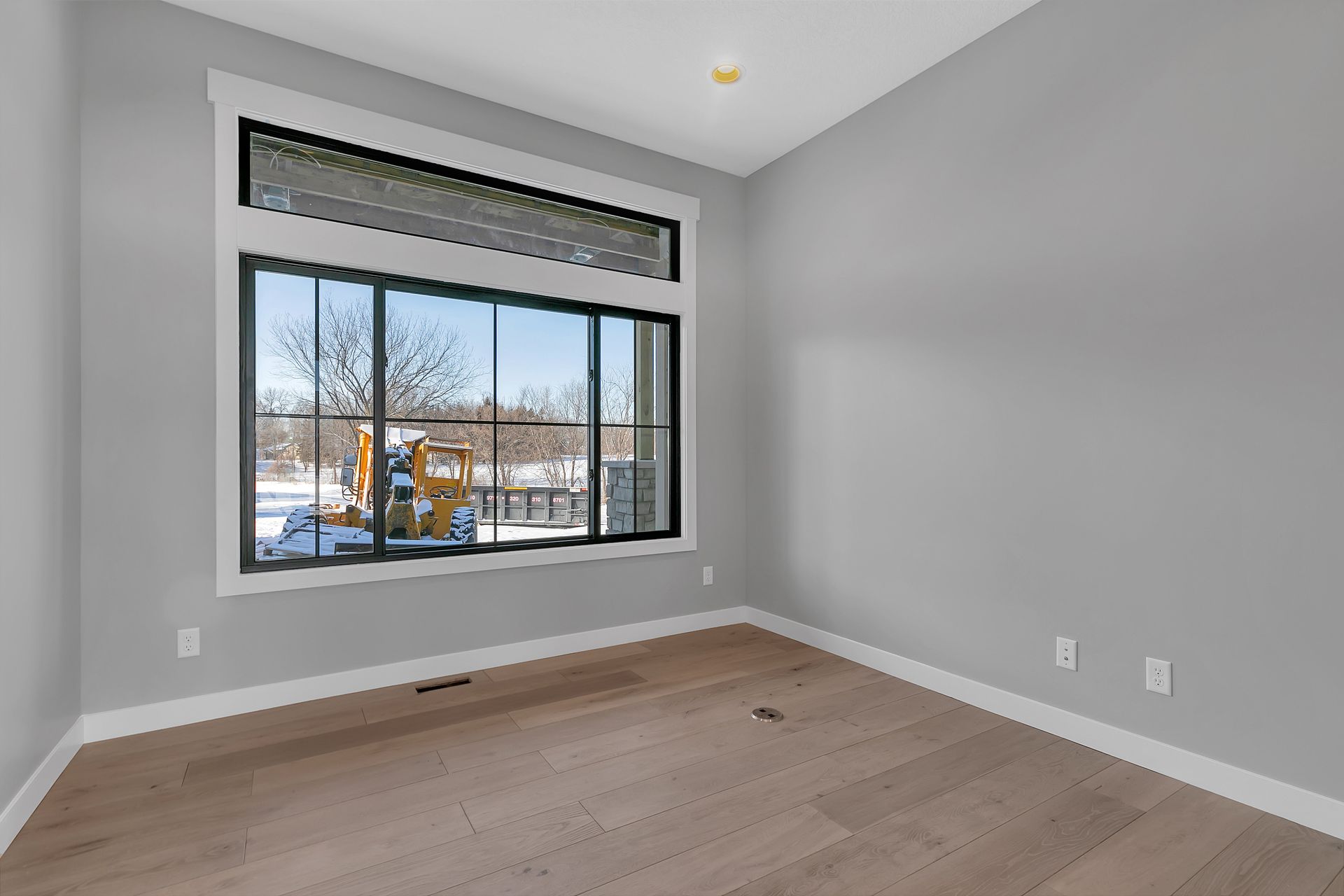 An empty room with a large window and hardwood floors.