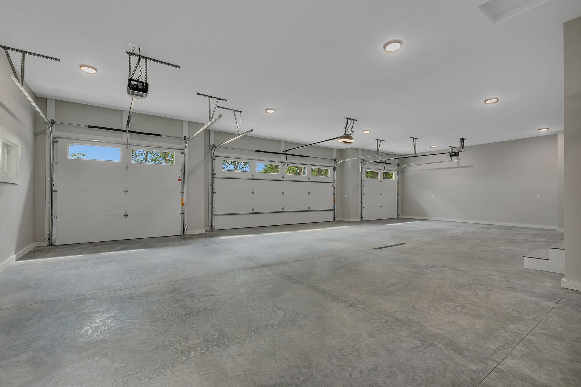 A large empty garage with three garage doors and a ceiling fan.