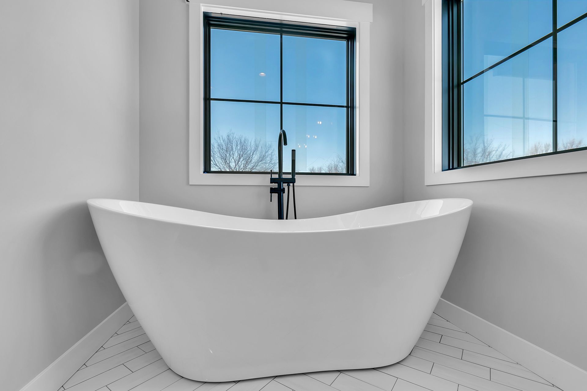 A white bathtub is sitting in the corner of a bathroom next to a window.