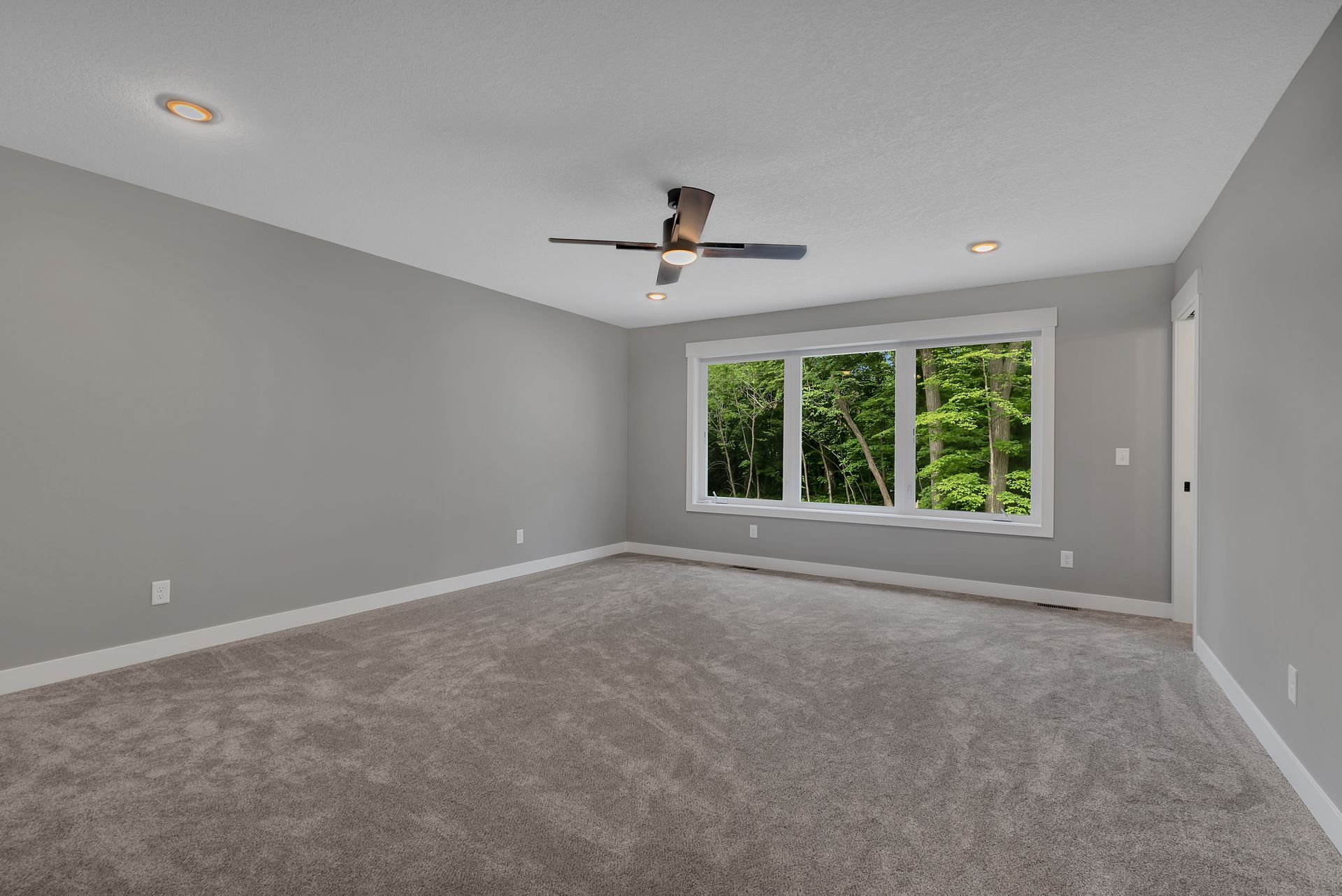 An empty room with a ceiling fan and three windows.