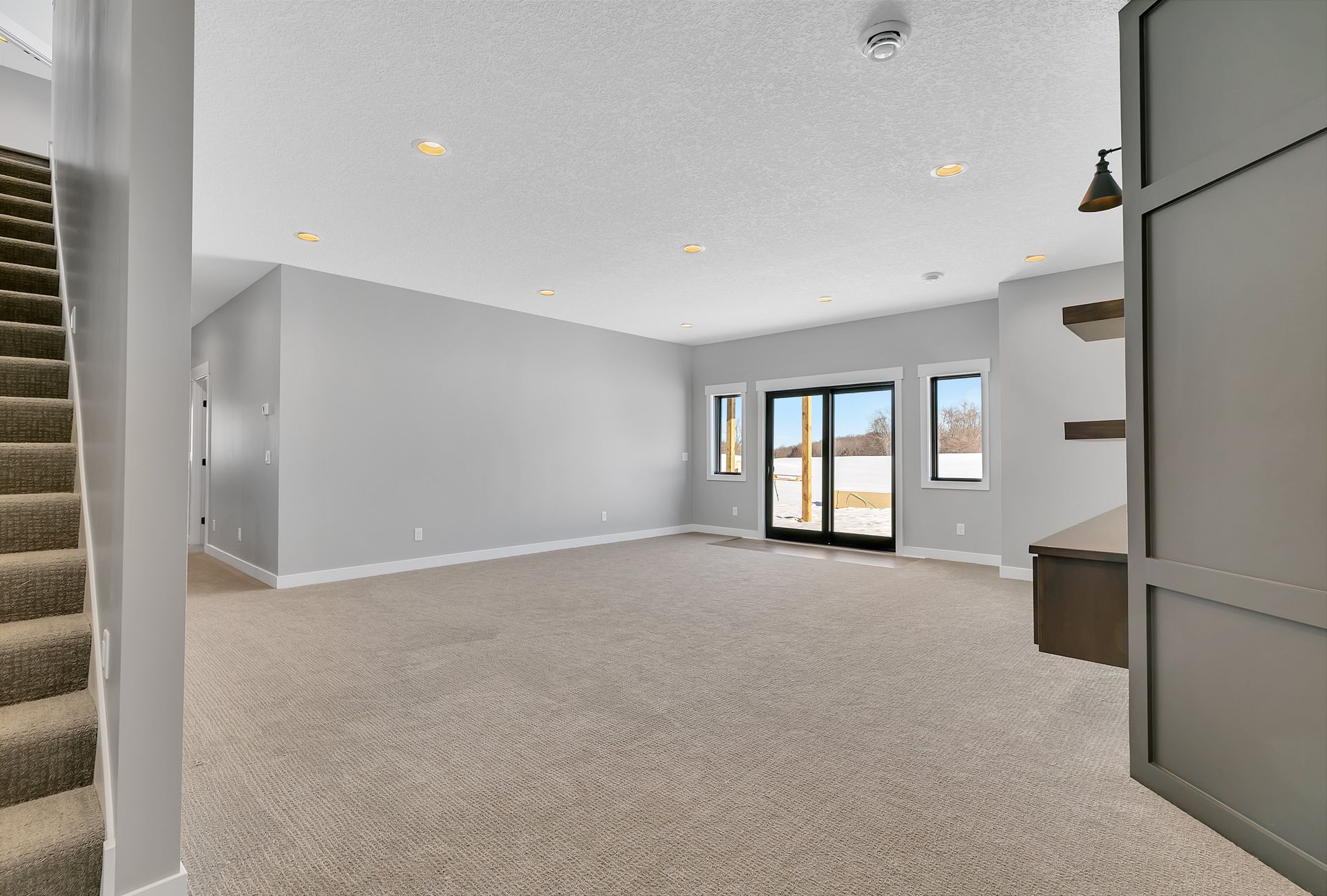 An empty basement with a staircase and sliding glass doors.