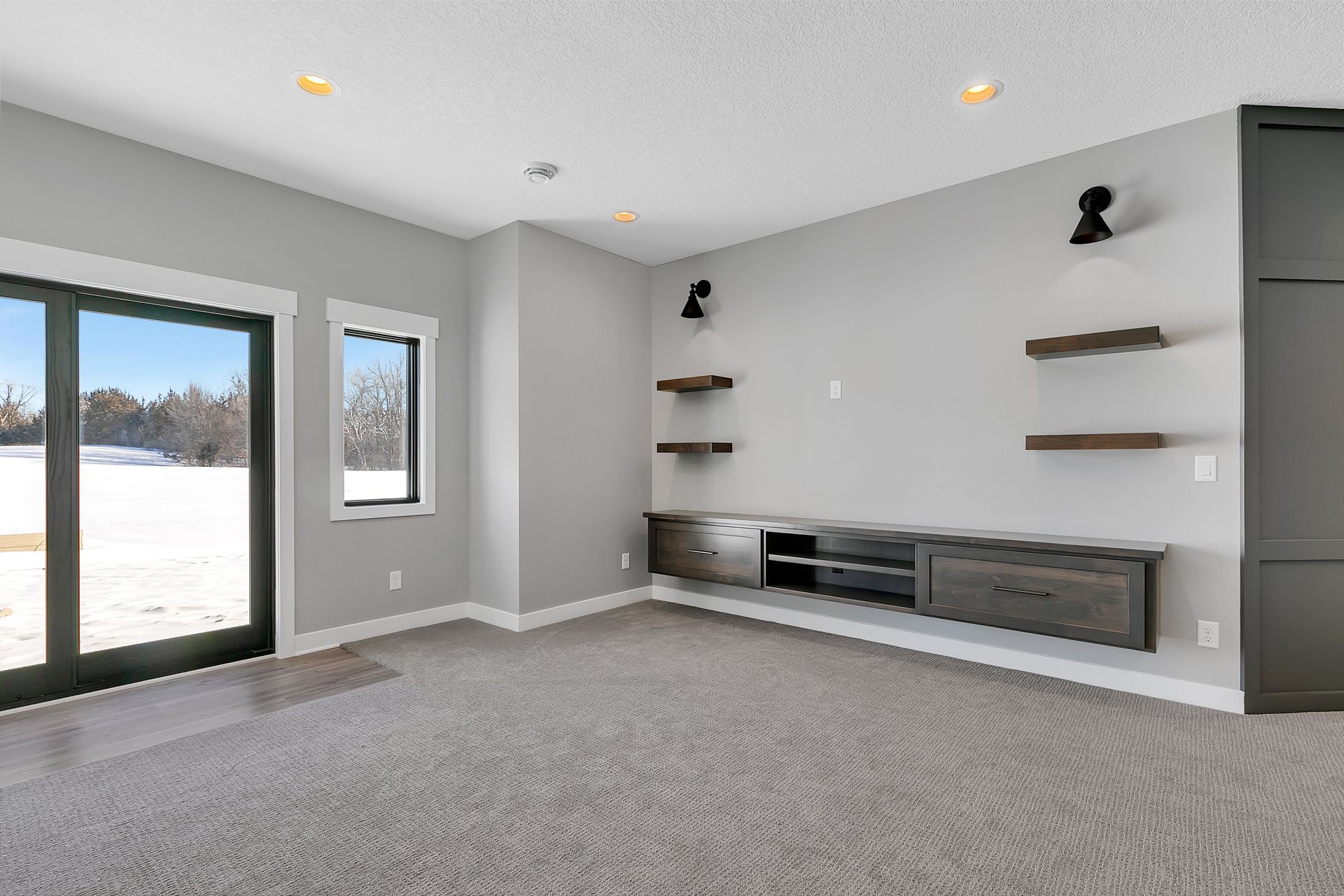 An empty living room with a sliding glass door and shelves.