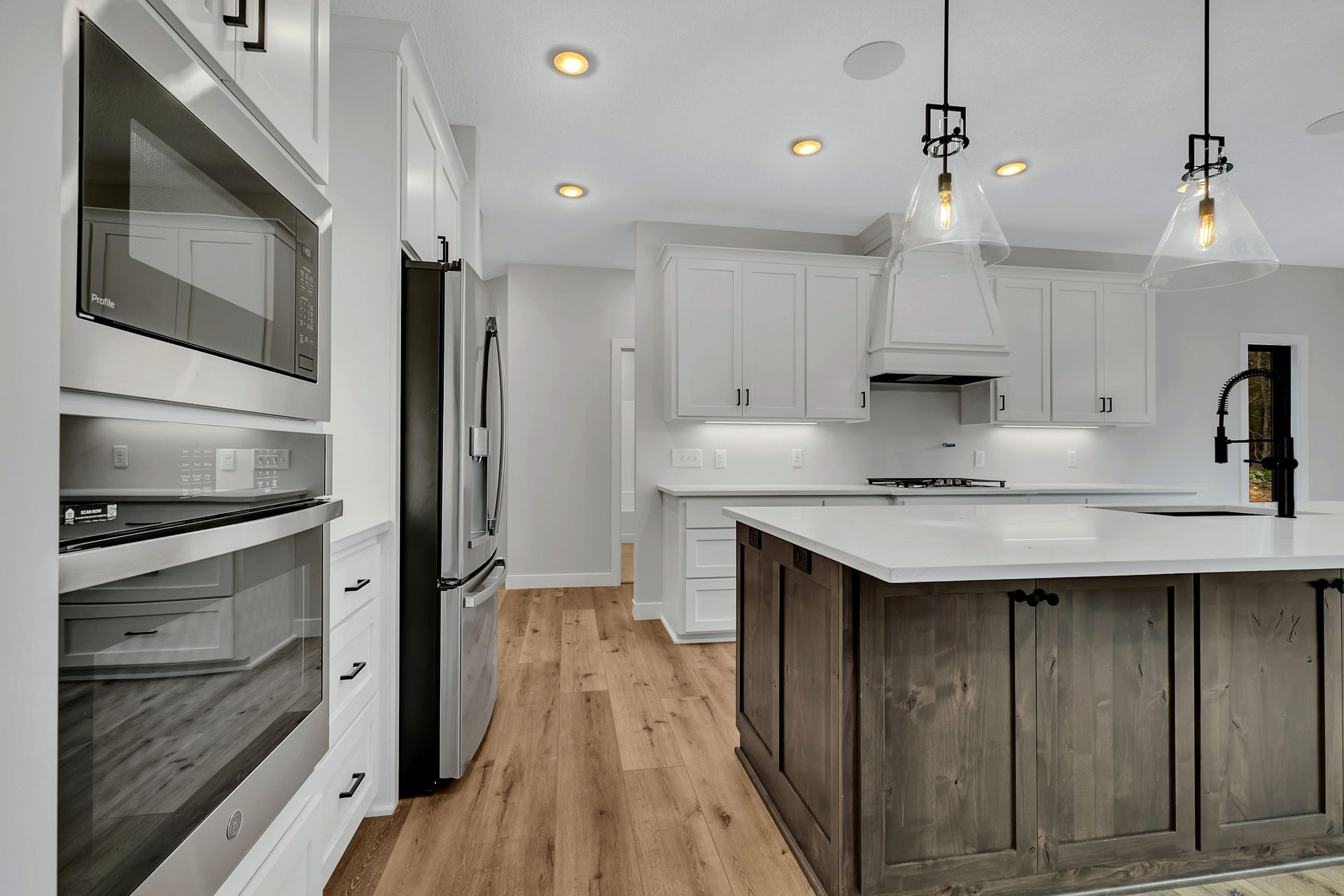 A kitchen with white cabinets , stainless steel appliances , a large island , and hardwood floors.