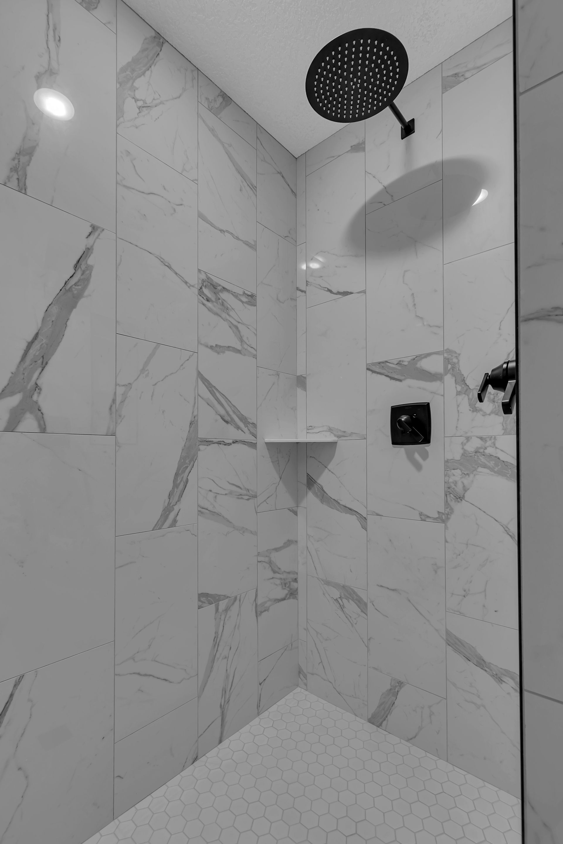 A black and white photo of a shower with marble tiles and a shower head.